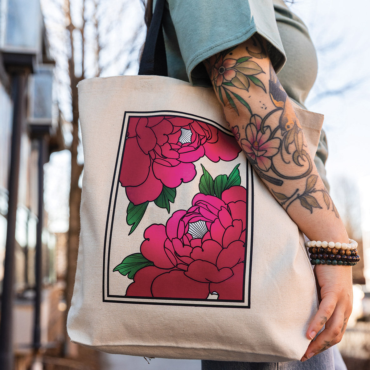 photo à l'extérieur d'une jeune femme tatouée portant un t-shirt vert et un sac fourre-tout imprimé avec des fleurs