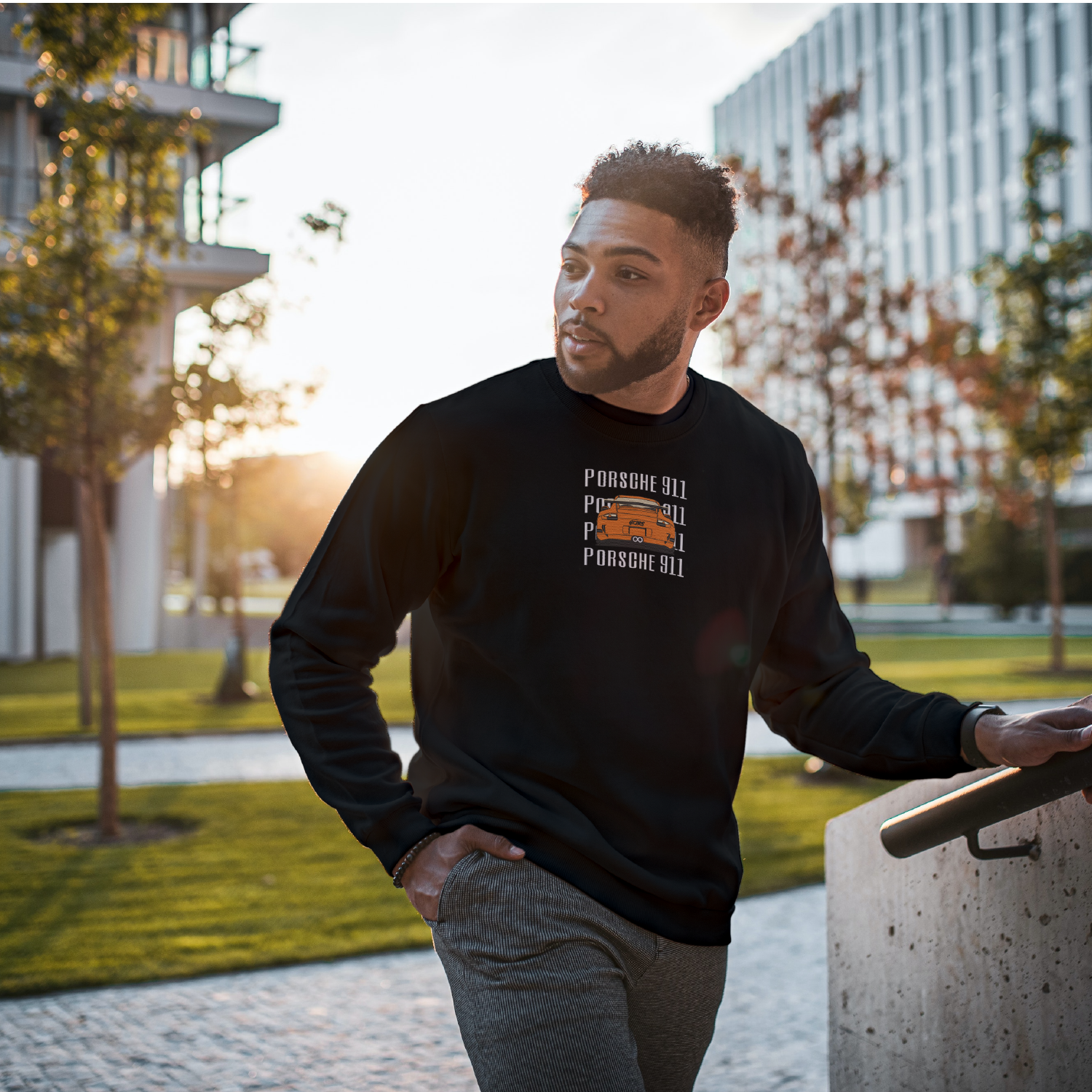 photo d'un jeune homme portant un crewneck brodame noir avec une porsche 911 orange