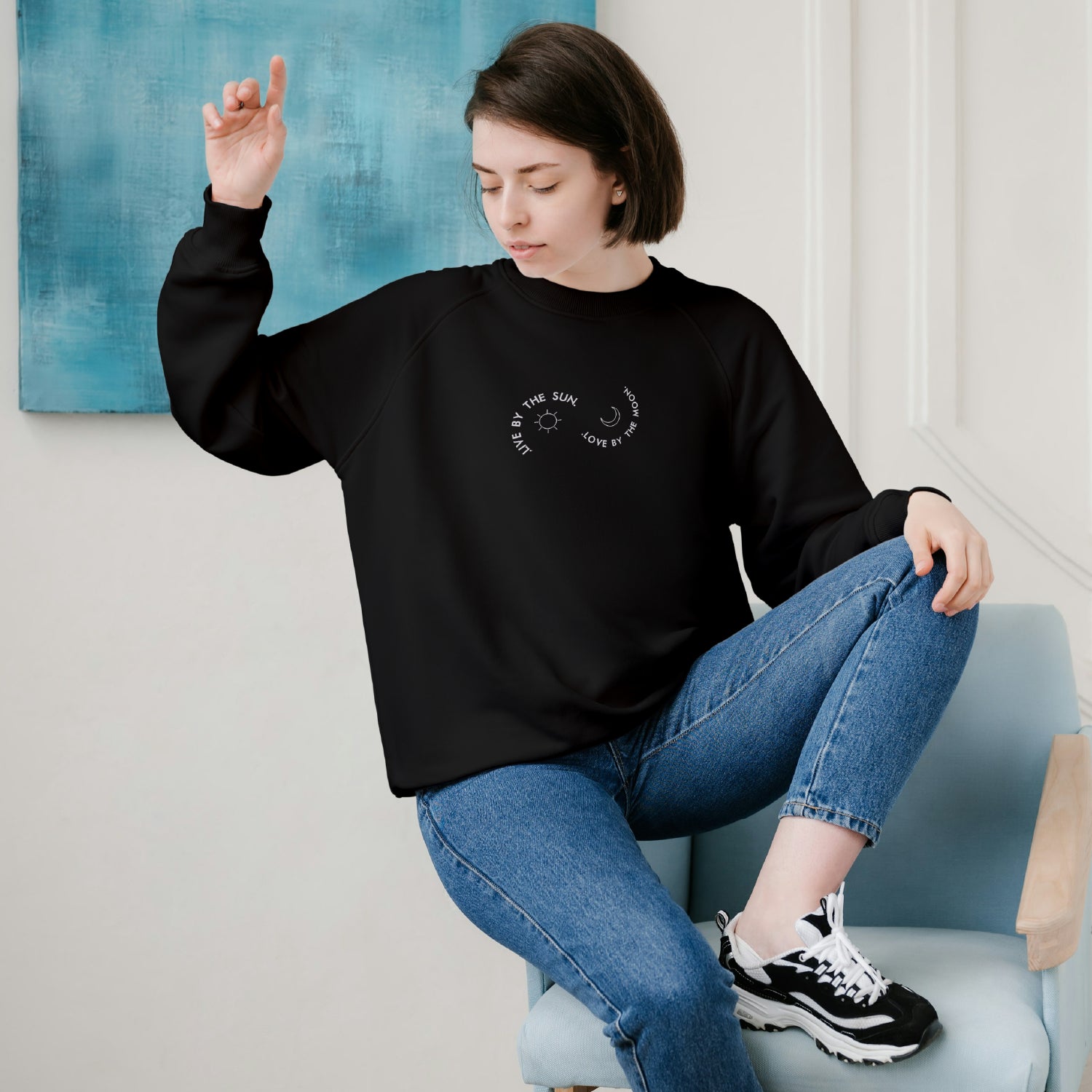 photo d'une jeune femme portant un crewneck noir brodé live by the sun love by the moon avec une lune et un soleil blancs