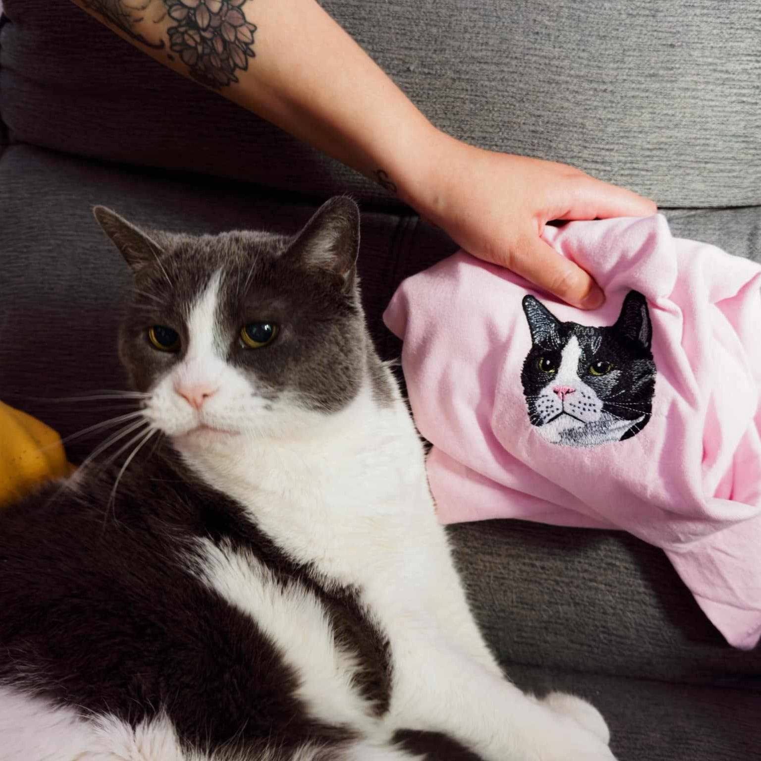 photo d'un t-shirt brodé avec un visage de chat avec le chat à côté du t-shirt pour voir le réalisme de la broderie
