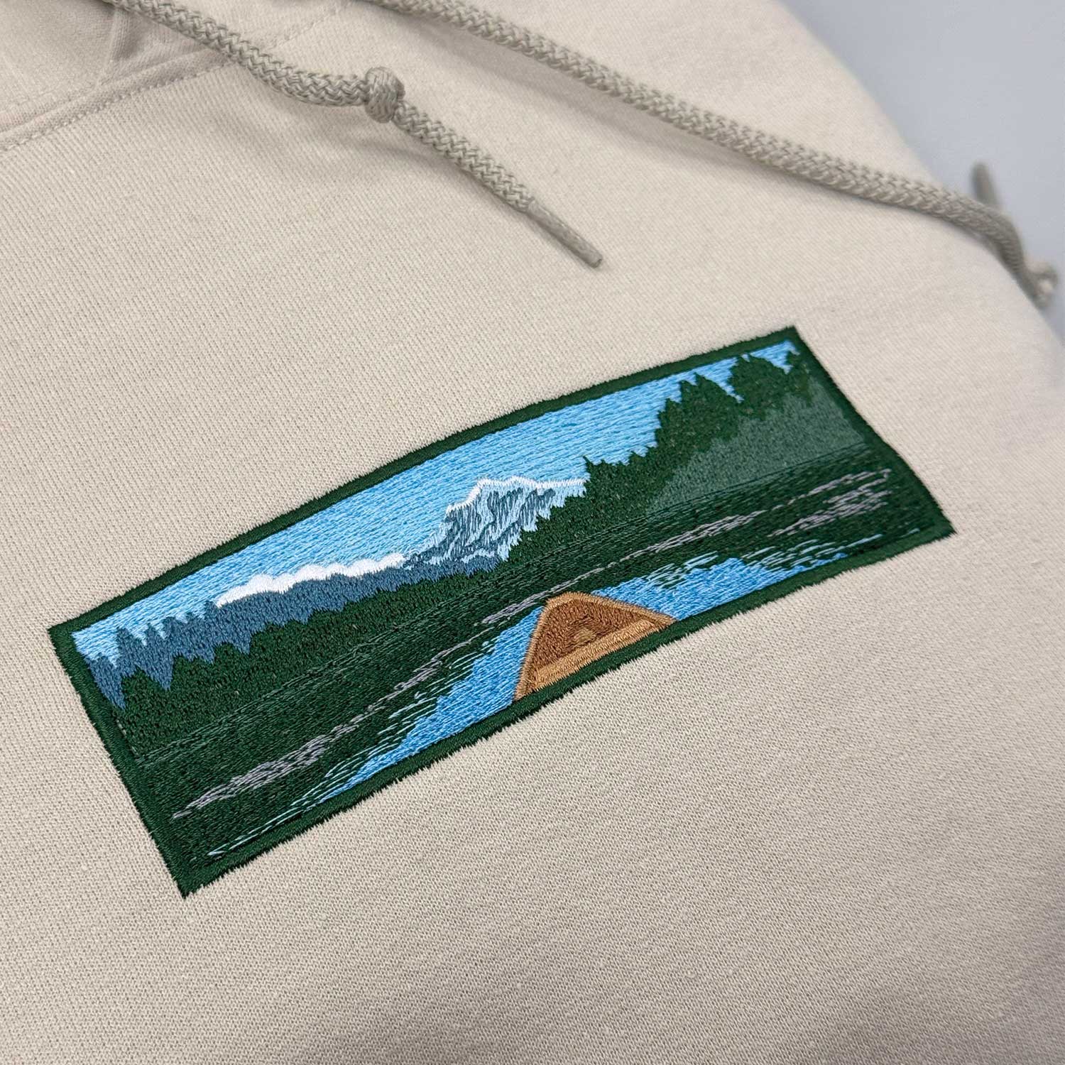 photo plan rapproché d'un hoodie à capuchon beige avec une broderie d'un canot dans une rivière