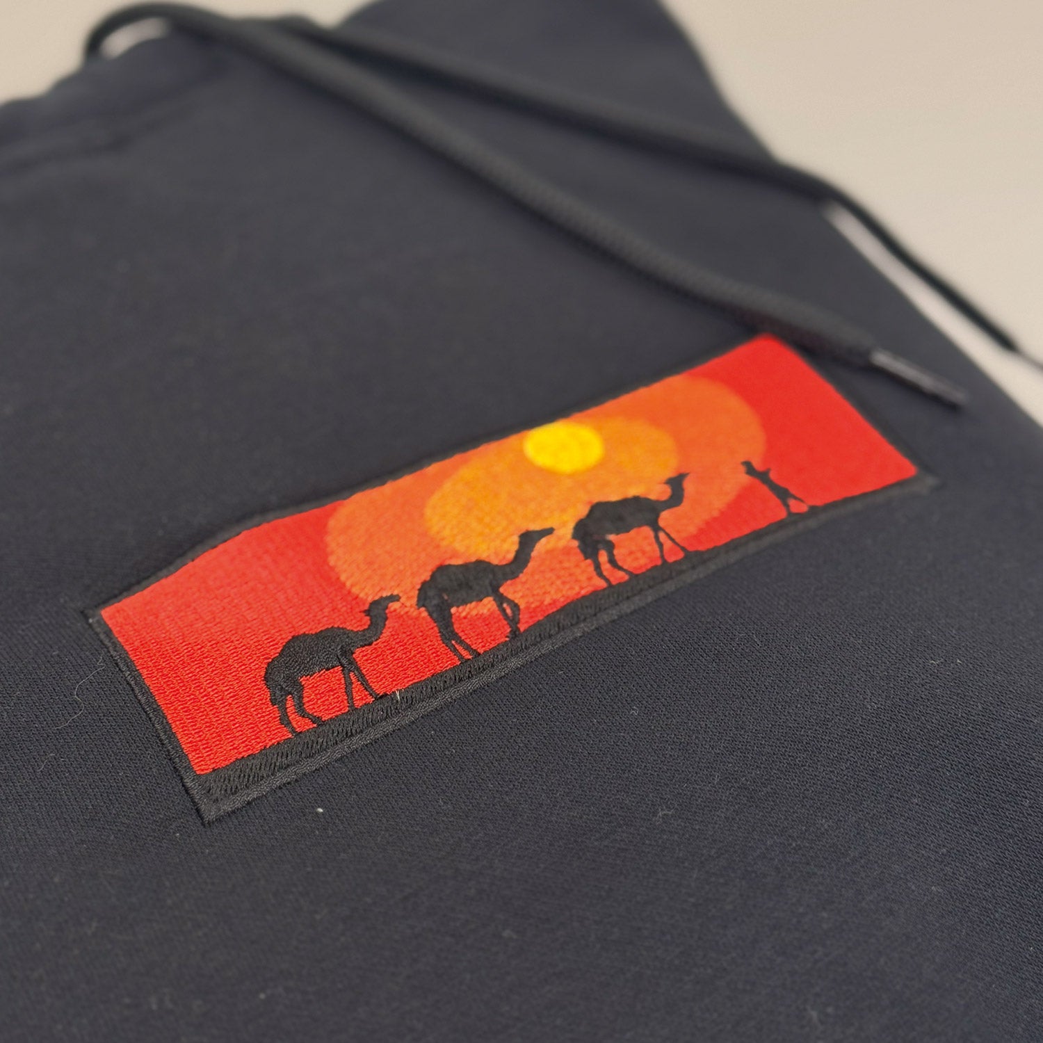 photo d'un plan rapproché d'un coton ouaté à capuchon noir avec une broderie d'un coucher de soleil dans le désert avec des chameaux