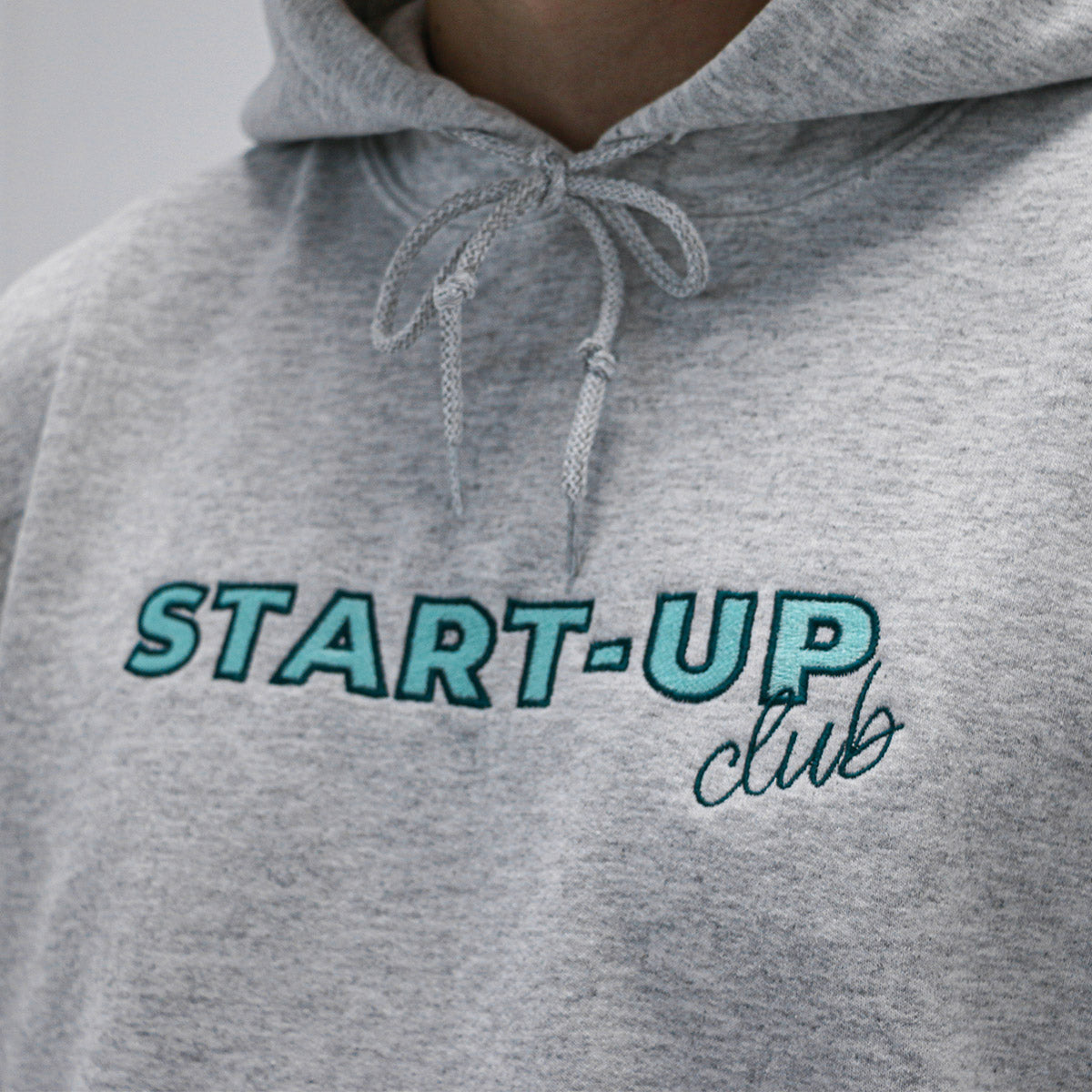 plan rapproché d'un coton ouaté à capuchon ayant une broderie "start-up club" au centre en turquoise pâle, contour foncé