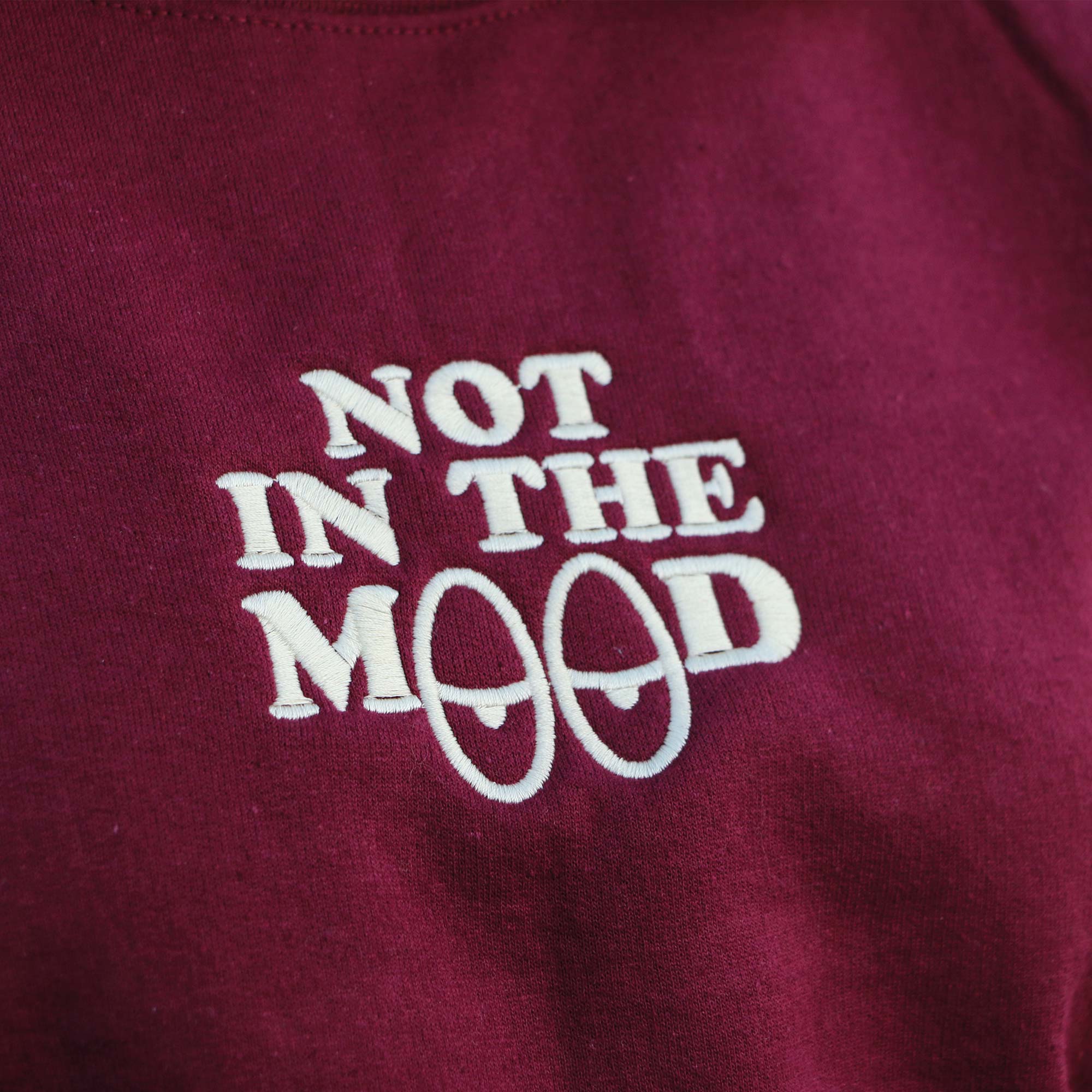 photo plan rapproché d'un crewneck bourgogne avec une broderie avec l'écriture "not in the mood" en blanc cassé