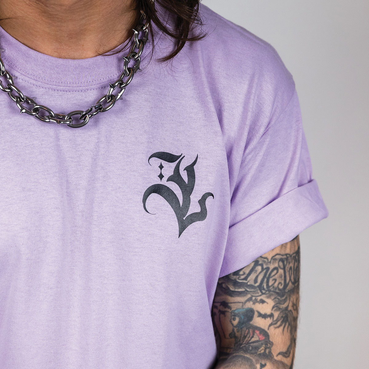 photo de plan rapproché du t-shirt lavande avec impression au coeur noir sur un mannequin homme tatoué