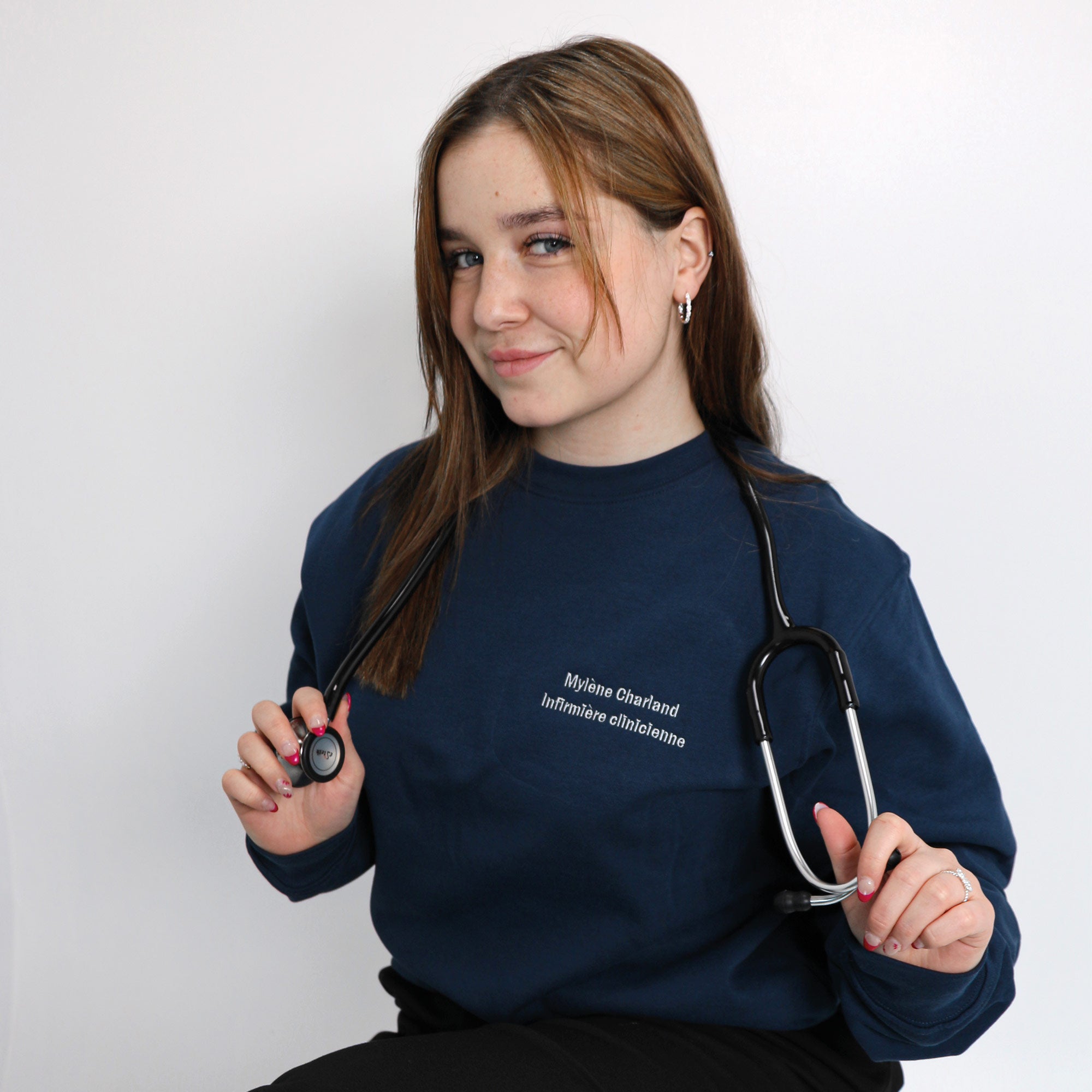 photo dans un studio d'une jeune femme infirmière portant un crewneck identifié avec son nom et sa profession et un stéthoscope autour du cou