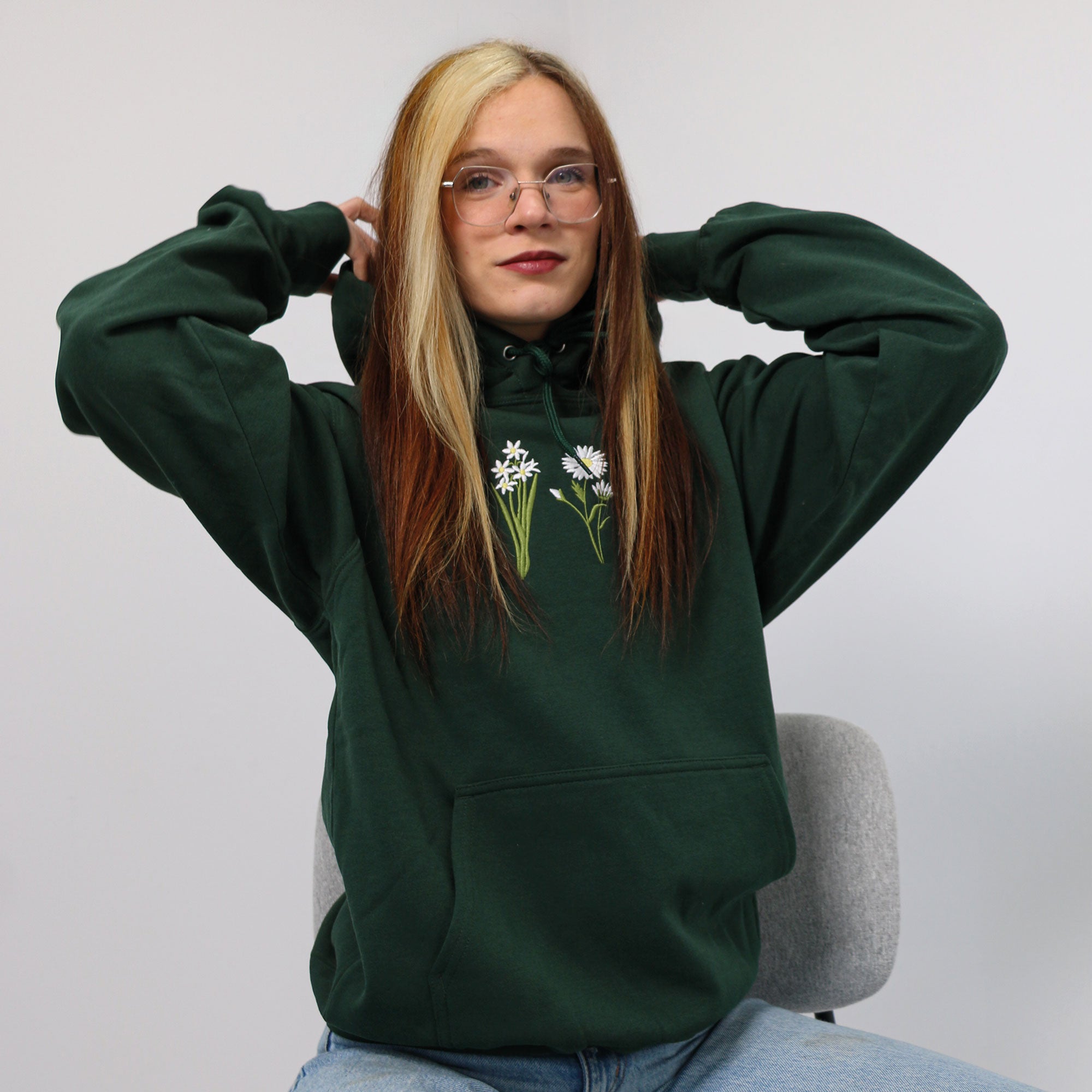 photo d'une jeune femme aux cheveux colorés portant un coton ouaté à capuchon vert foret avec des fleurs de naissance de membres de sa famille