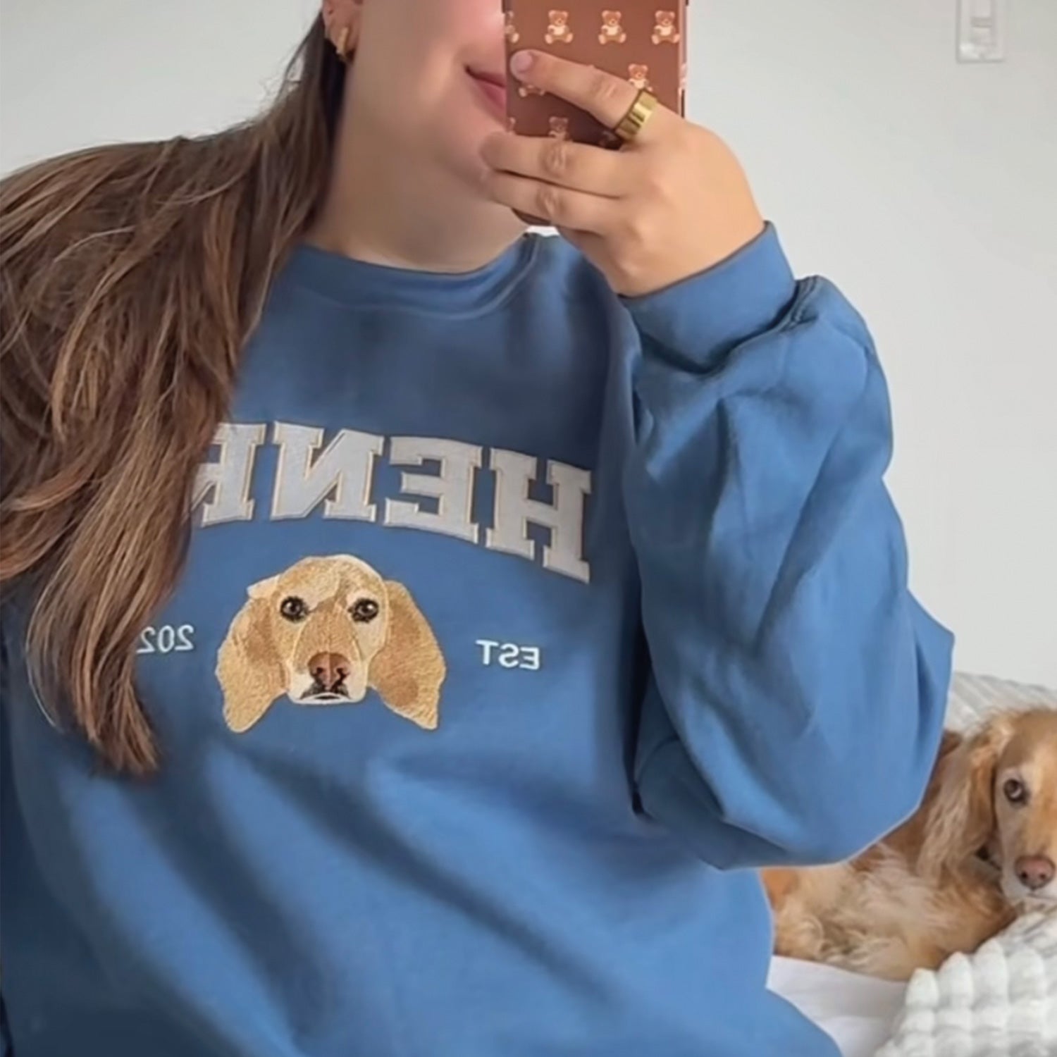 photo lifestyle d'une selfie dans le miroir d'une jeune femme aux cheveux longs bruns portant un crewneck bleu avec une broderie personnalisée de son chien