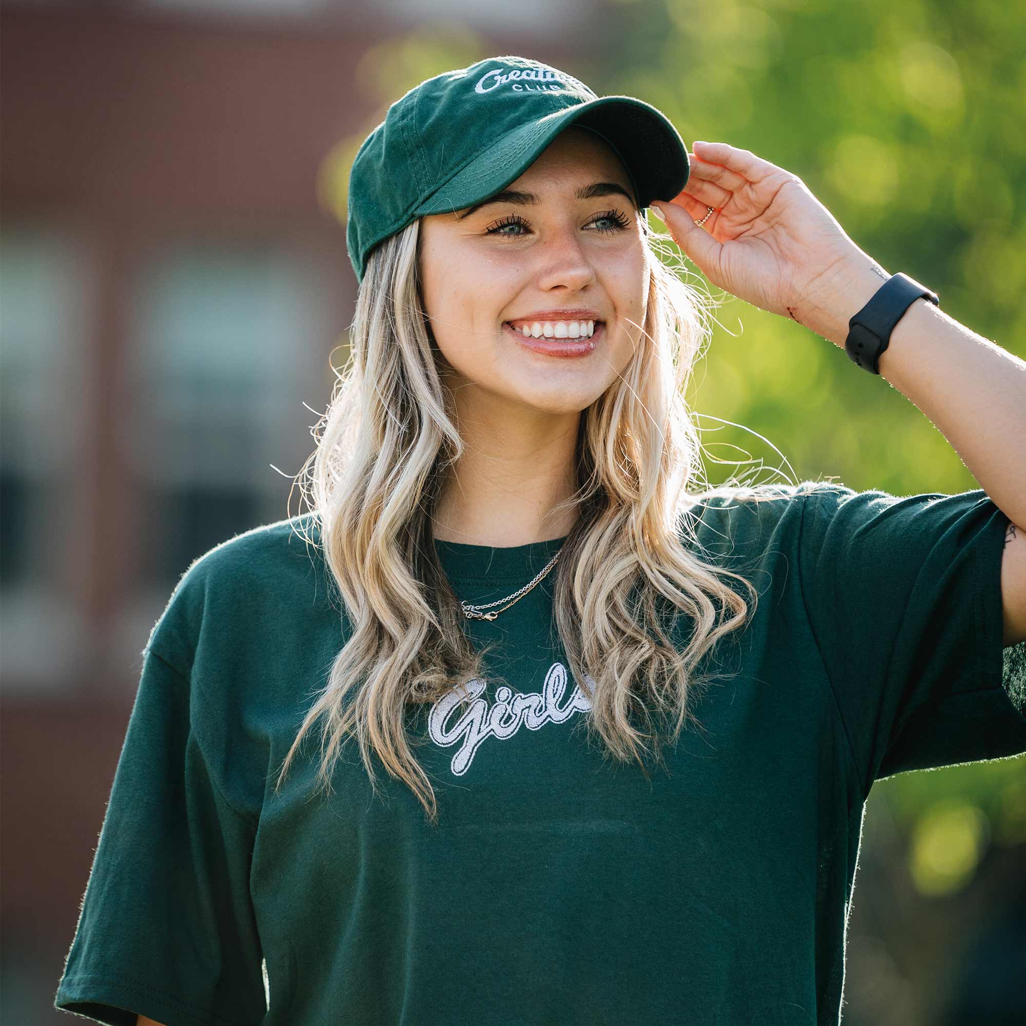 jeune femme blonde portant un t-shirt vert foret avec broderie girls et une casquette verte foret avec broderie creative club par brodame
