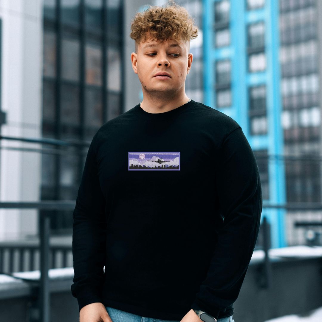 photo lifestyle d'un jeune homme portant un crewneck noir avec une broderie d'un décollage d'avion en soirée