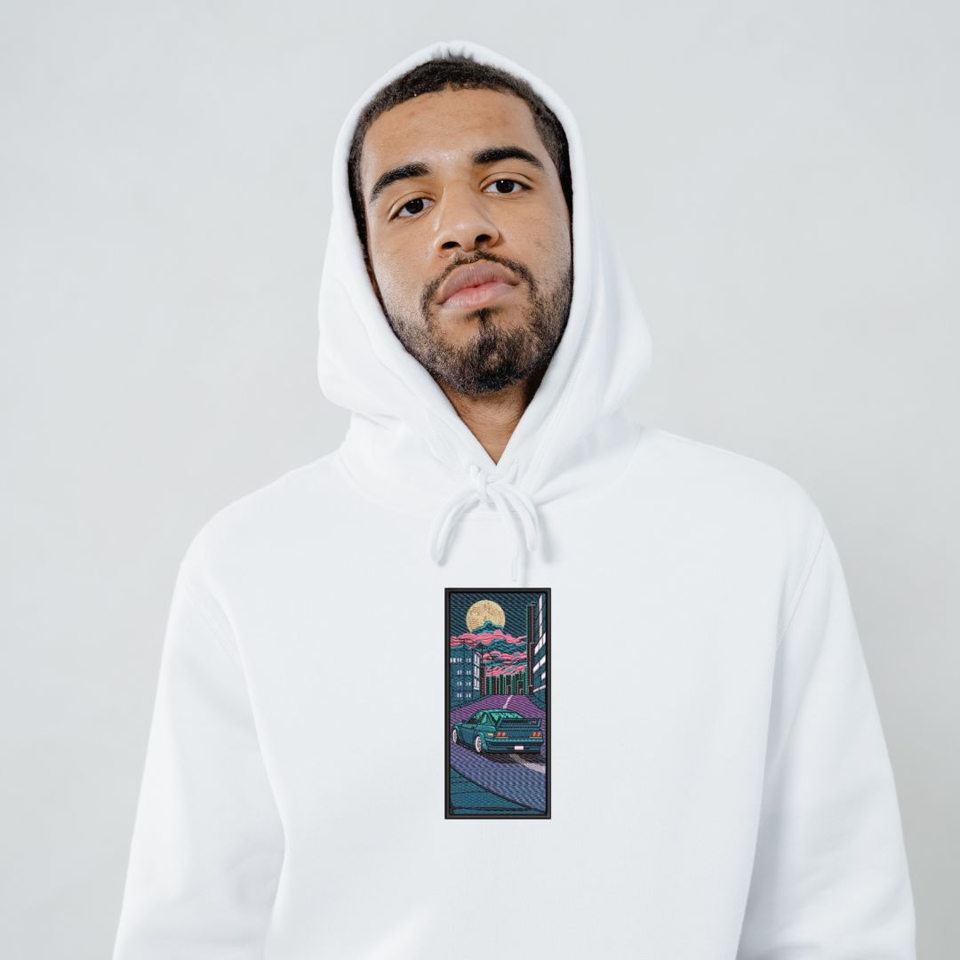 photo lifestyle d'un homme metis portant un coton ouaté à capuchon blanc avec une broderie détaillée d'une voiture JDM dans un paysage nocturne au japon