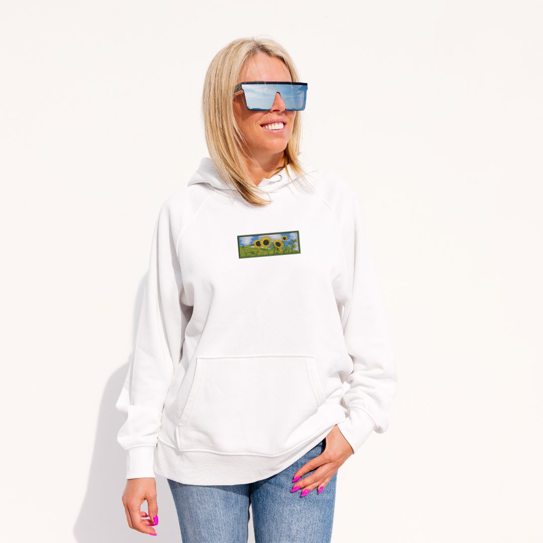 femme blonde avec des lunettes de soleil portant un hoodie blanc avec une broderie d'un champ de tournesols