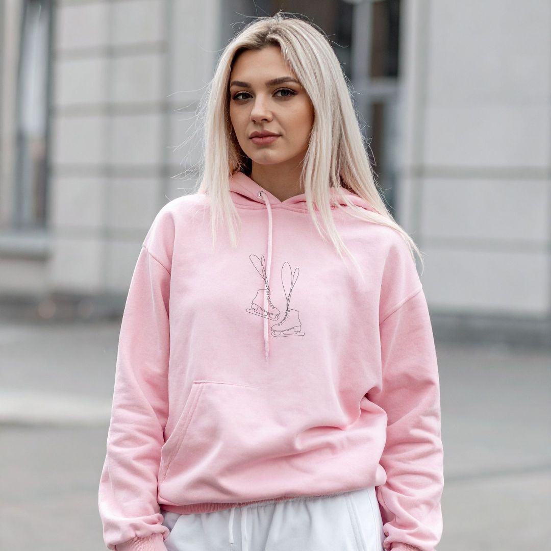 photo lifestyle d'une jeune femme blonde portant un coton ouaté à capuchon rose pâle avec une broderie minimaliste de patins de patinage artistique en noir