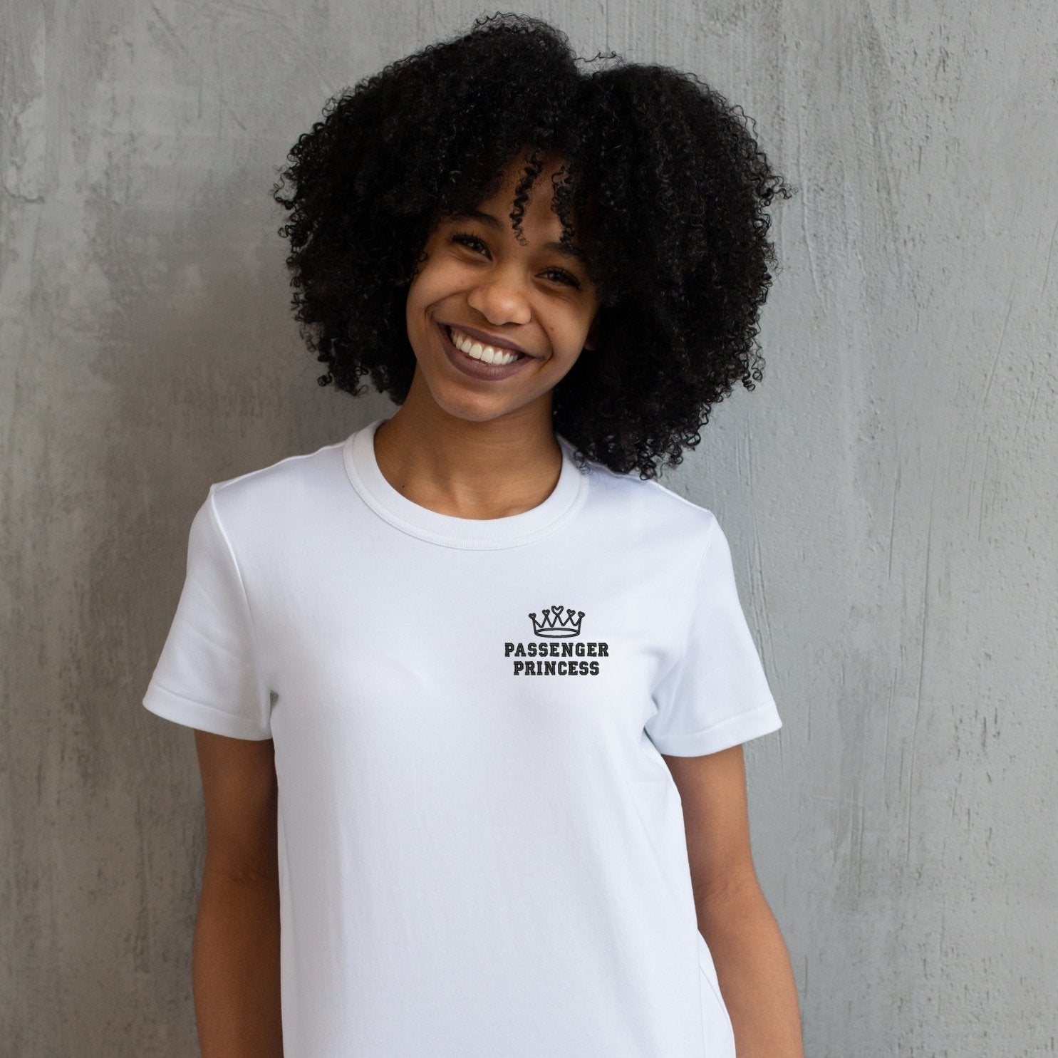 photo lifestyle d'une jeune femme afro-américaine souriante portant un t-shirt à manches courtes blanc avec une broderie "passenger princess" en noir au coeur.