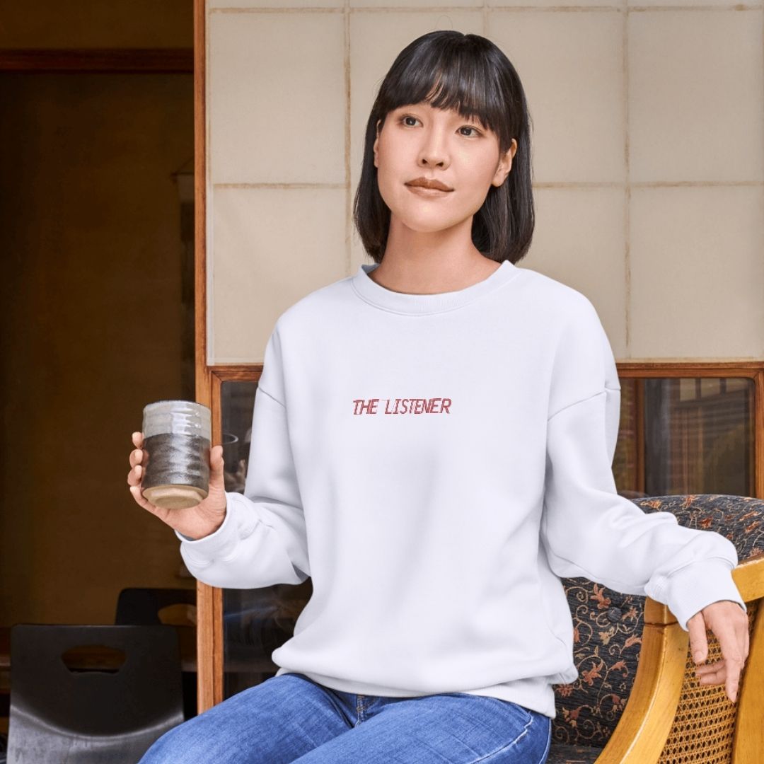 jeune fille asiatique portant un coton ouaté à col rond "the listener" brodé en rouge en tenant un verre dans ses mains