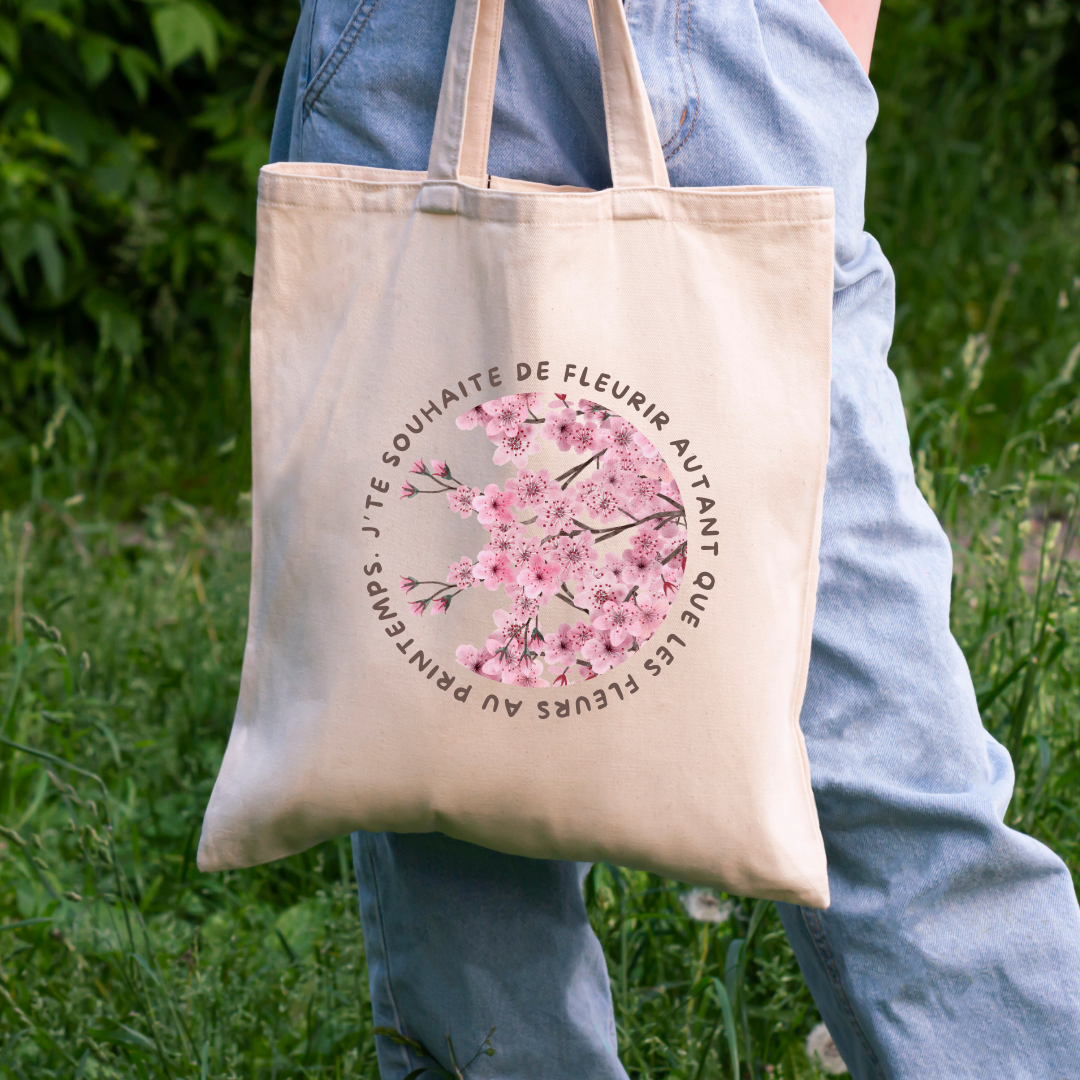 photo d'une femme transportant un sac fourre-tout beige avec une impression de fleurs cherry blossoms et une phrase inspirante française dans un champ
