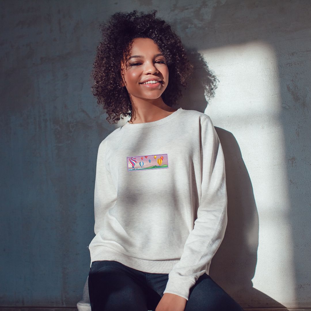 photo lifestyle d'une jeune femme noire portant un crewneck blanc avec un paysage de montgolfières