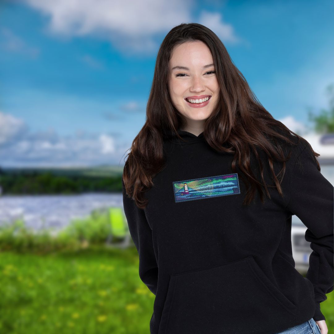 photo lifestyle d'une jeune femme brune portant un hoodie noir avec une broderie détaillée d'un phare sur le bord de la mer pendant la nuit
