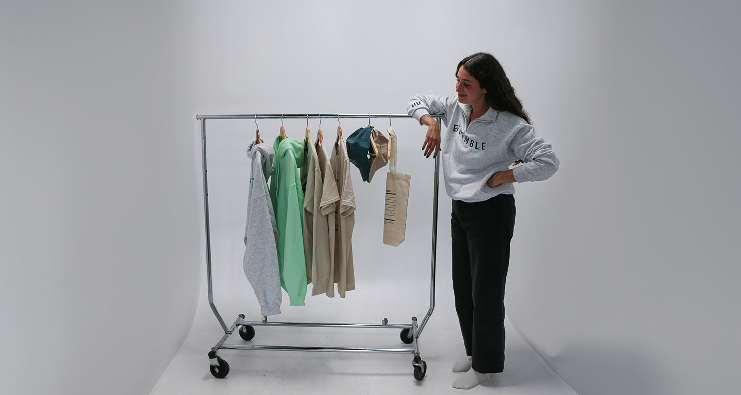 photo d'un rack de vêtements ayant la collection brodame X acee. Une jeune femmes aux cheveux longs bruns est accotée sur le rack et regarde les différents morceaux brodés et imprimé. le tout sur un fond de cyclorama blanc