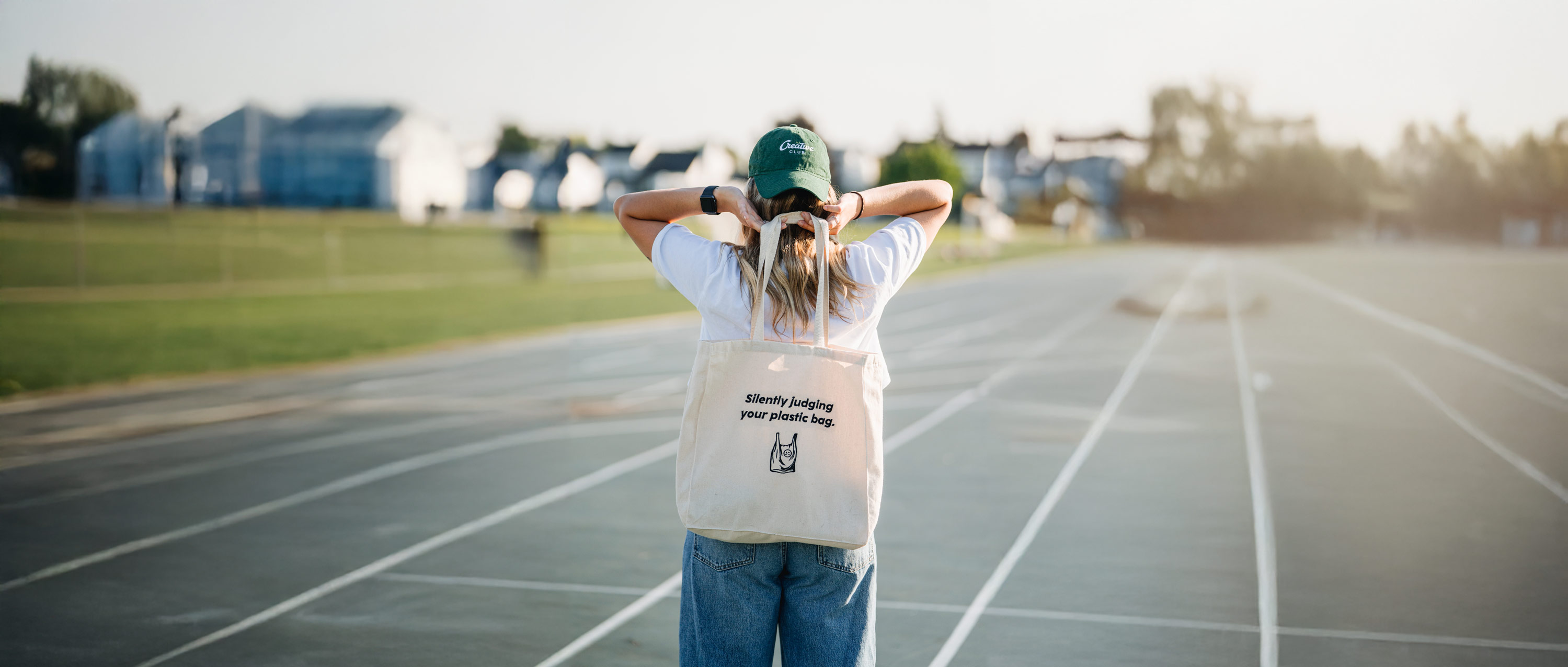 photo d'une jeune femme sur un terrain d'athletisme portant une casquette verte brodée et un sac fourre-tout brodé en noir