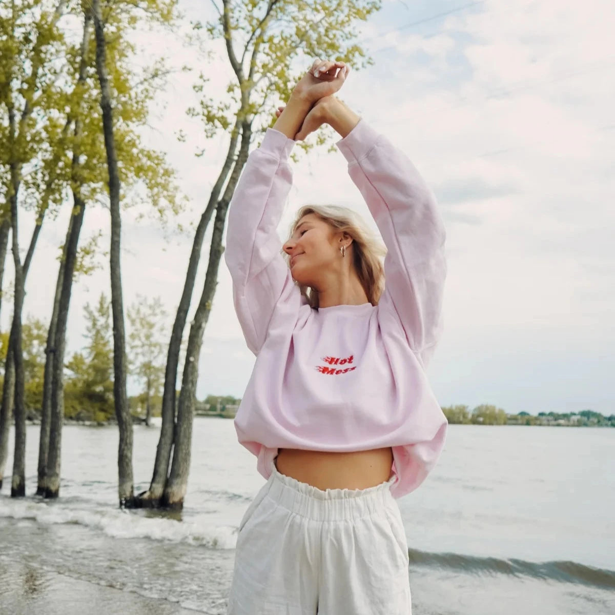 jeune femme portant un crewneck rose pâle sur le bord de l'eau avec une broderie Hot Mess en rouge