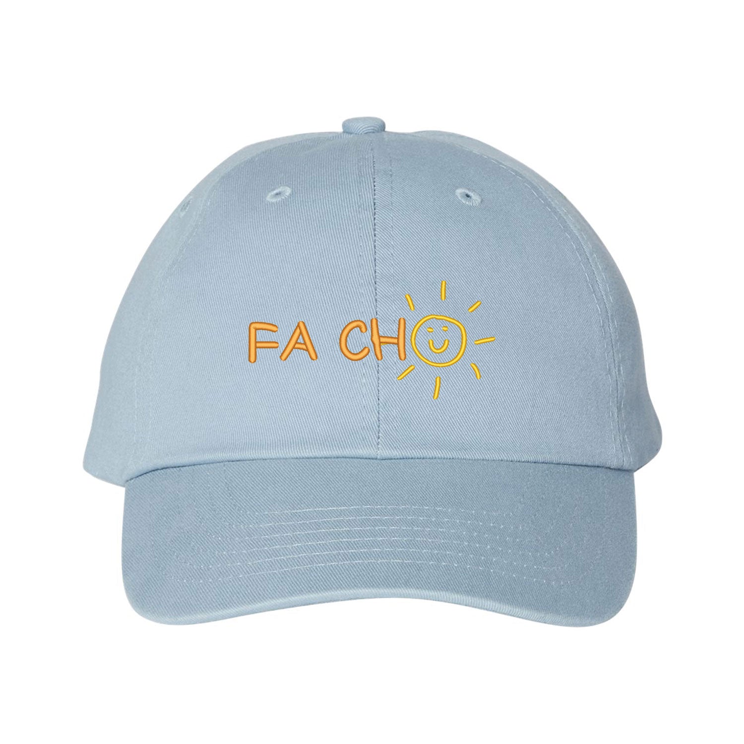 Casquette bleu pâle brodée "Fa cho". La broderie se trouve centrée sur la casquette à l'avant. Les lettres "FA CH" sont brodés de couleur orange pâle et le "O" est un soleil avec un bonhomme sourire de couleur jaune. Collection d'expressions québécoises du 29 juin 2025.