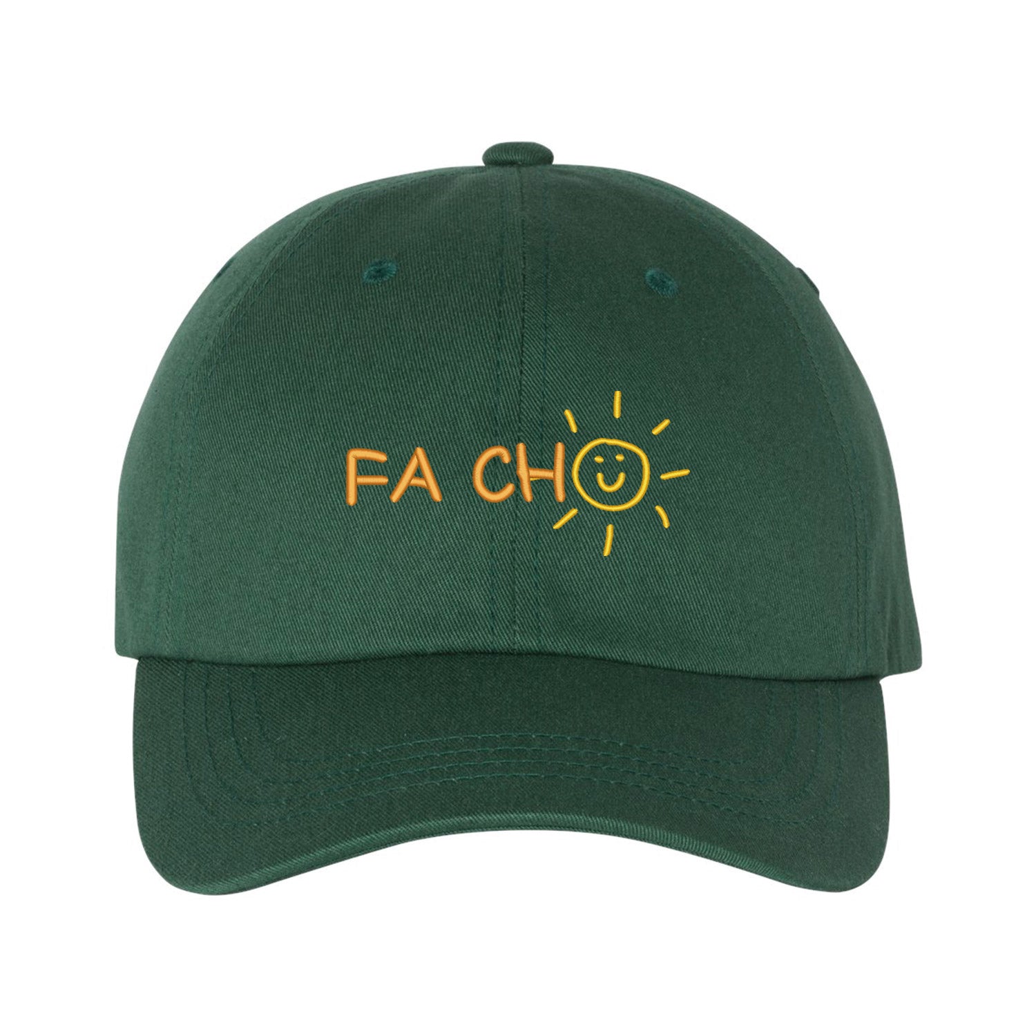 Casquette vert forêt brodée "Fa cho". La broderie se trouve centrée sur la casquette à l'avant. Les lettres "FA CH" sont brodés de couleur orange pâle et le "O" est un soleil avec un bonhomme sourire de couleur jaune. Collection d'expressions québécoises du 29 juin 2025.