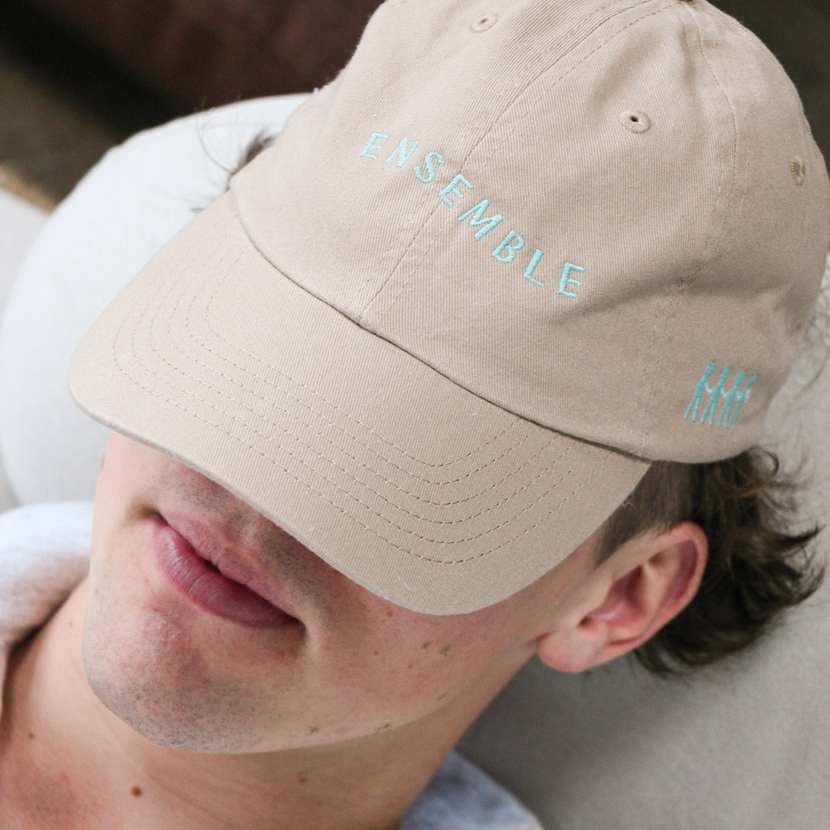 plan rapproché d'un jeune homme portant une casquette beige avec une broderie "ensemble" sur le devant, 4 bonhommes allumettes se tenant la main sur le côté. brodé en tuquoise pâle.