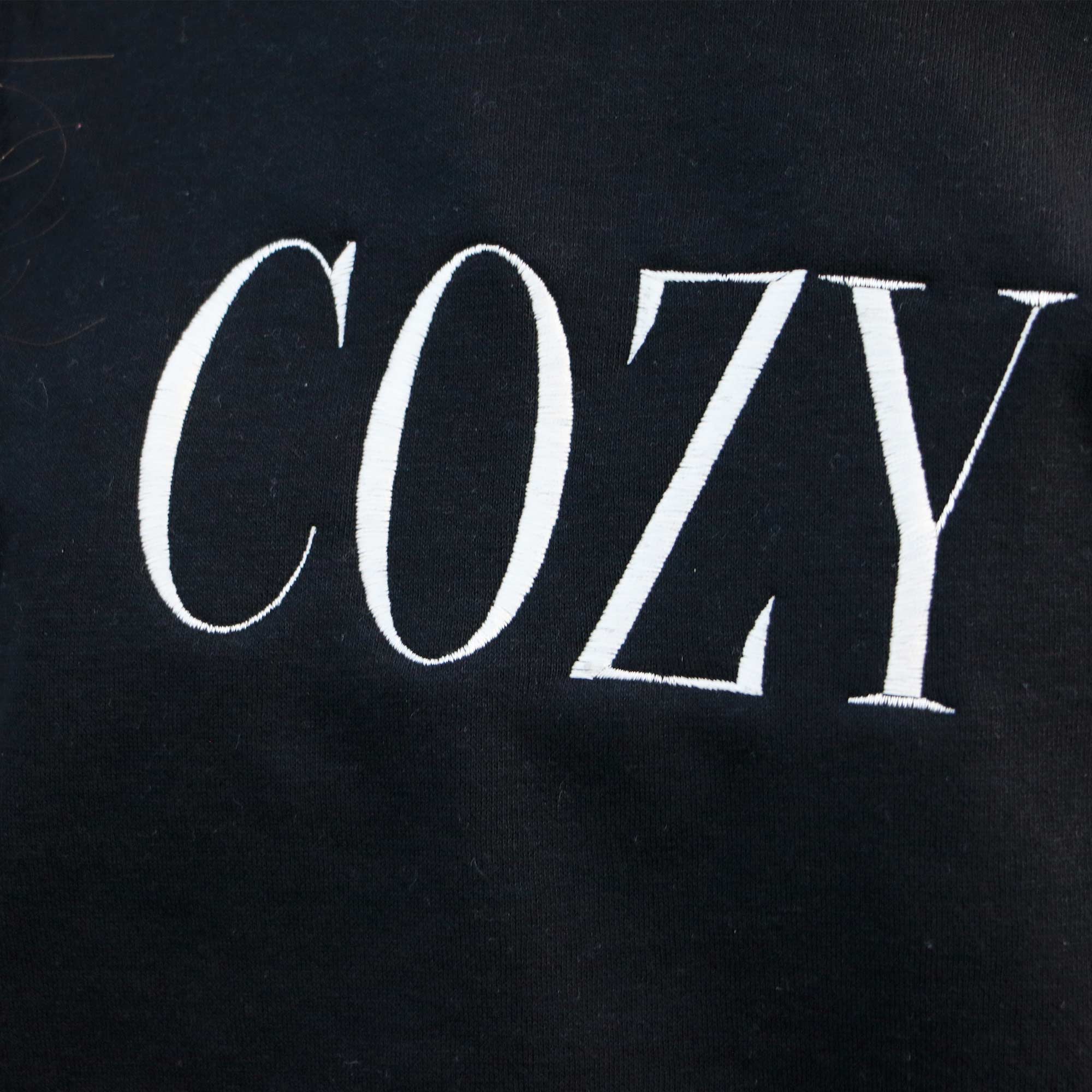 photo plan rapproché d'un crewneck brodé avec le mot cozy en blanc crème