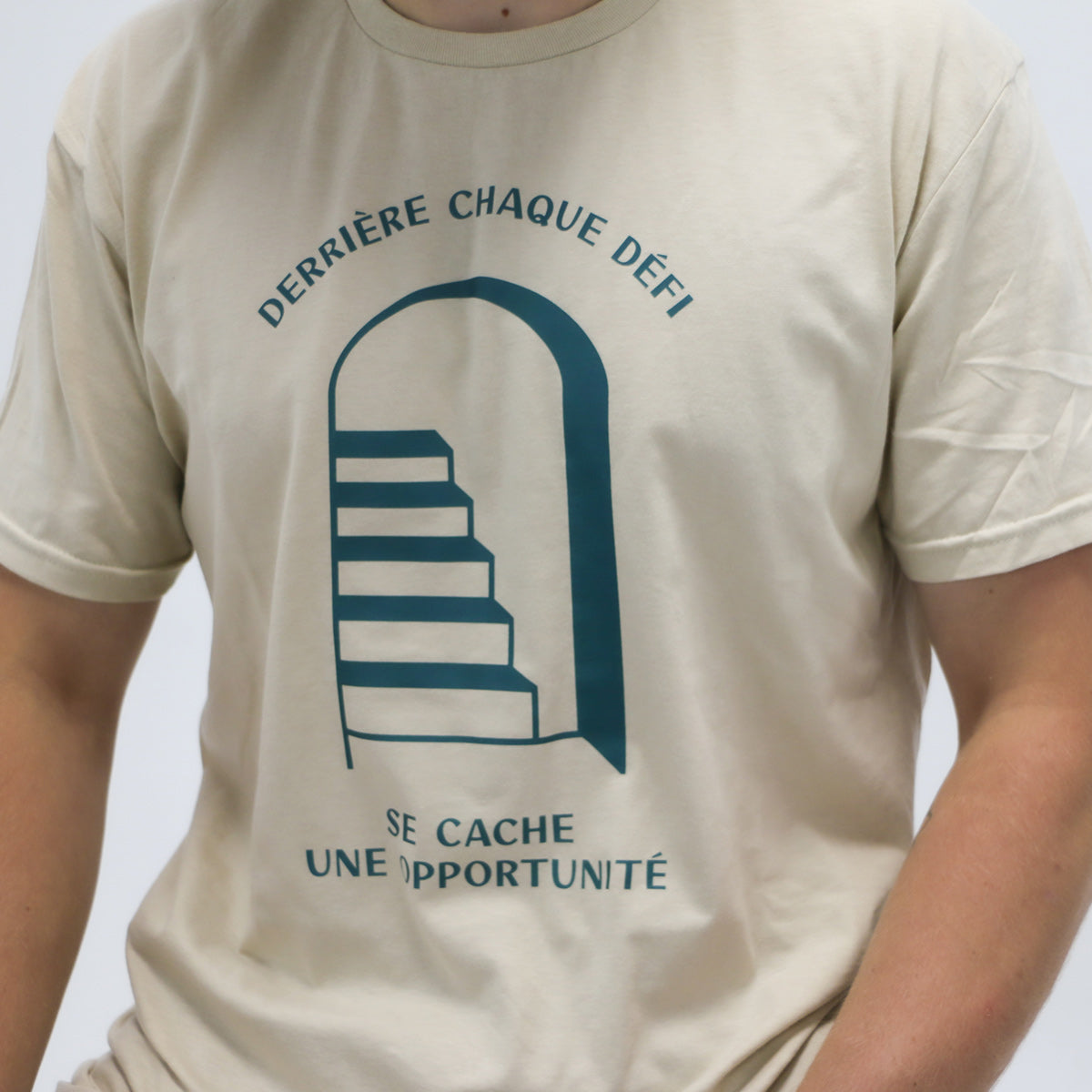 photo de plan rapproché d'un jeune homme portant un t-shirt beige avec la phrase "derrière chaque défi se cache une opportunité" avec une cage d'escaliers en turquoise foncé