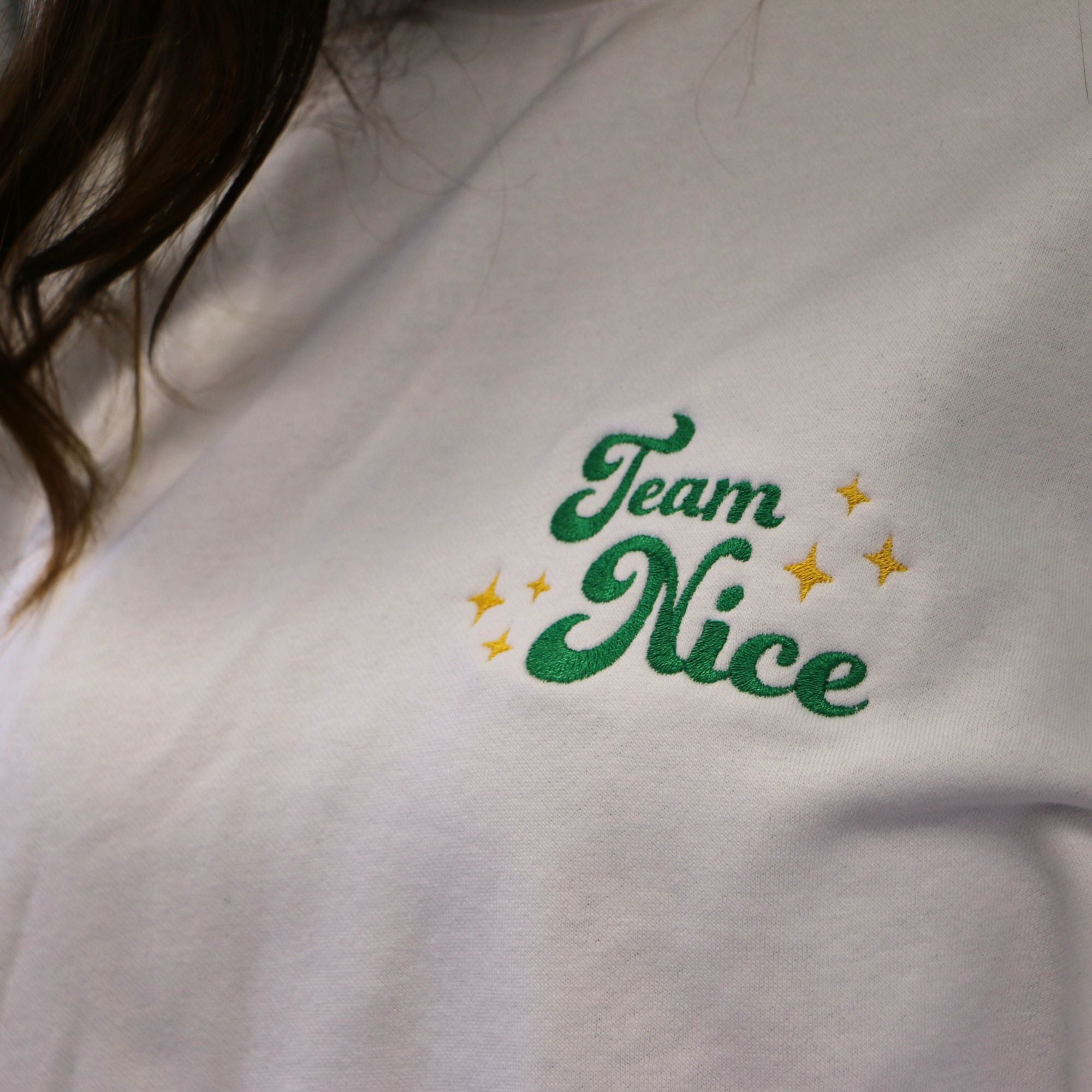 photo plan rapproché d'un crewneck blanc brodé avec l'écriture team nice avec des petites étoiles jaunes