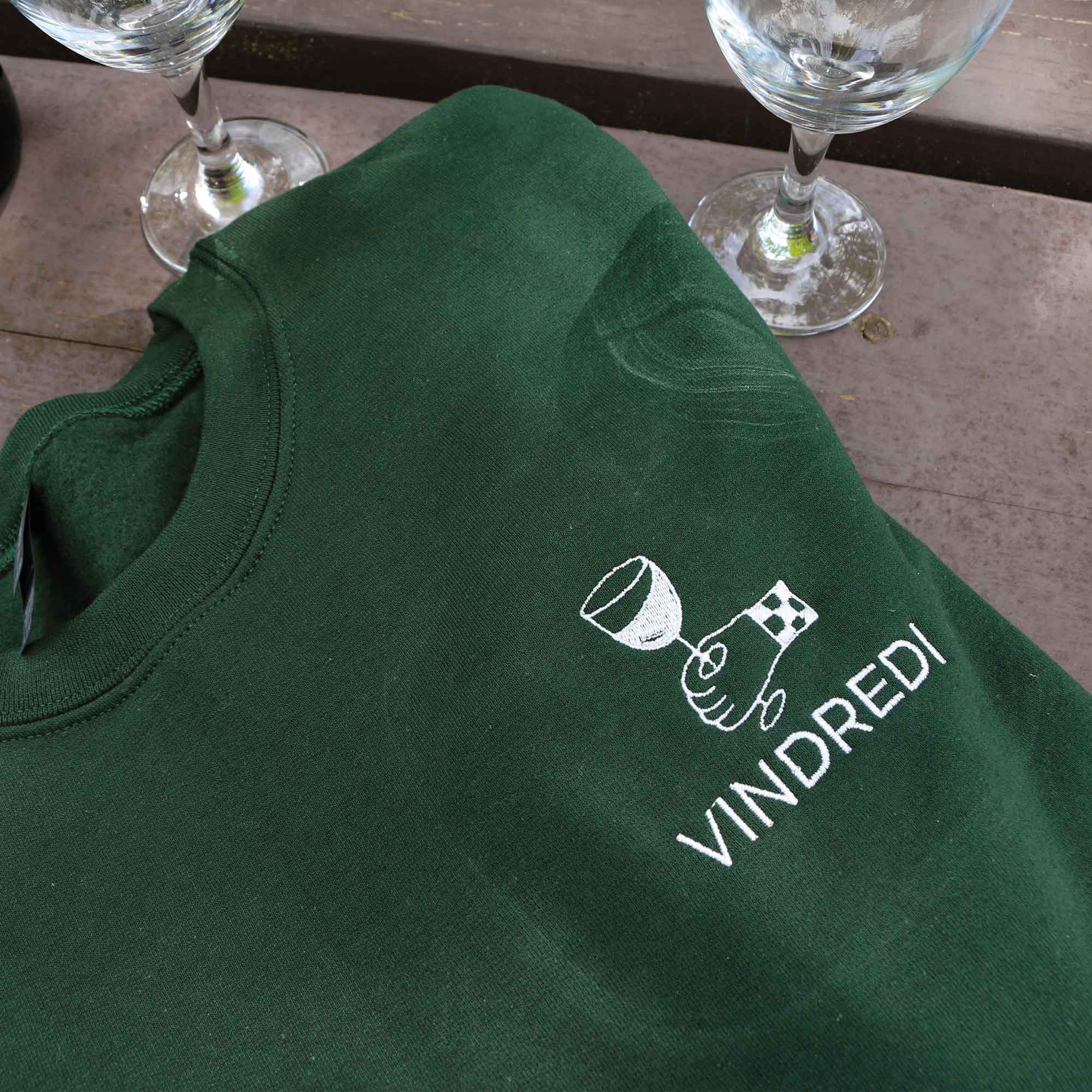 plan rapproché d'un crewneck vert foret avec une broderie blanche "vindredi" avec une coupe de vin au coeur. 