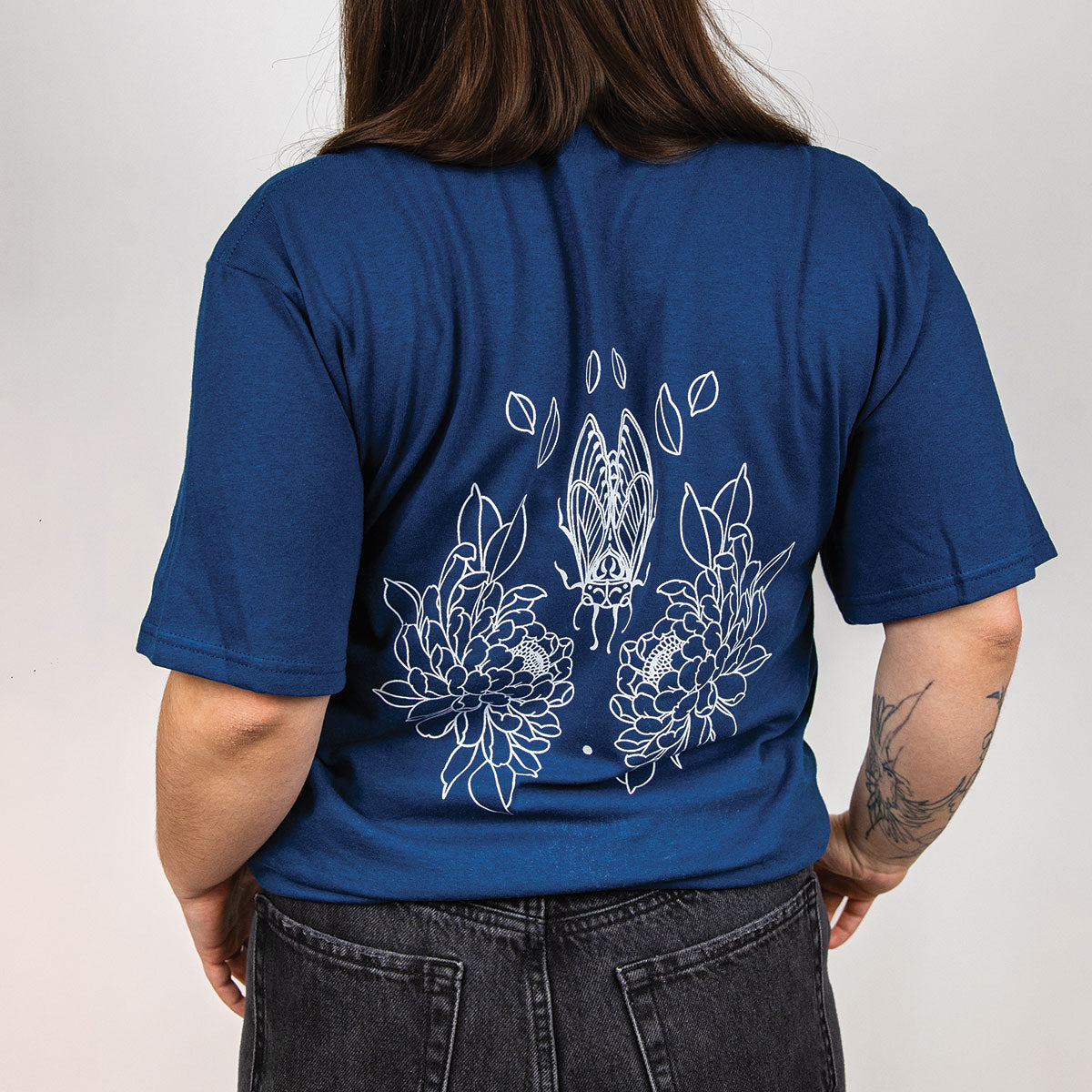 photo sur fond blanc d'une jeune femme de dos portant un t-shirt bleu neptune avec un imprimé de lignage botanique minimaliste