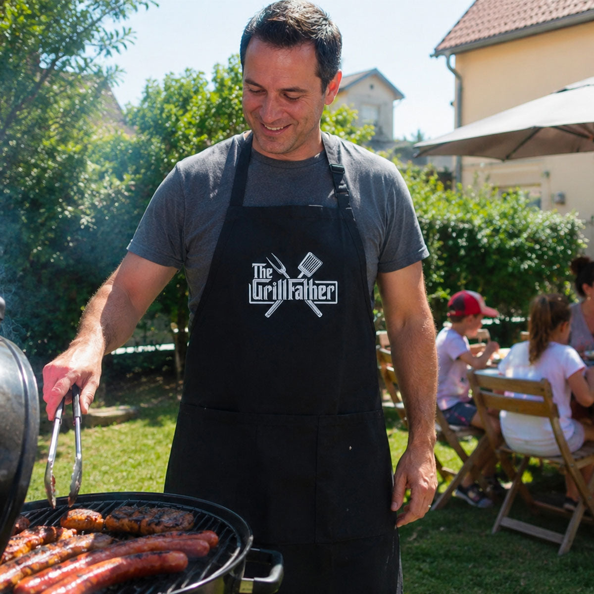 photo d'un père de famille qui fait des grillades sur un barbecue avec un tablier noir et une broderie "the grillfather"