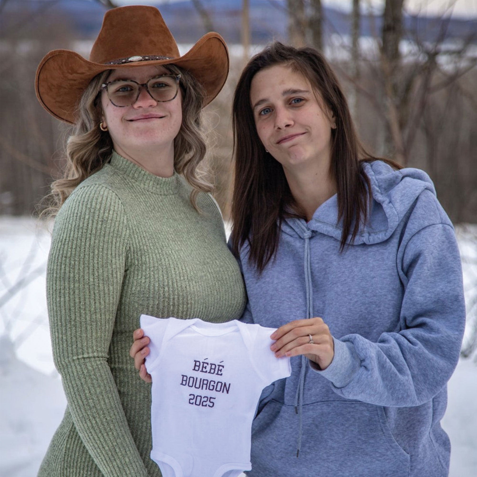 Photo lifestyle d'un couple de femme posant dehors en hiver avec un cache-couche blanc brodé personnalisé pour annoncer une grossesse.