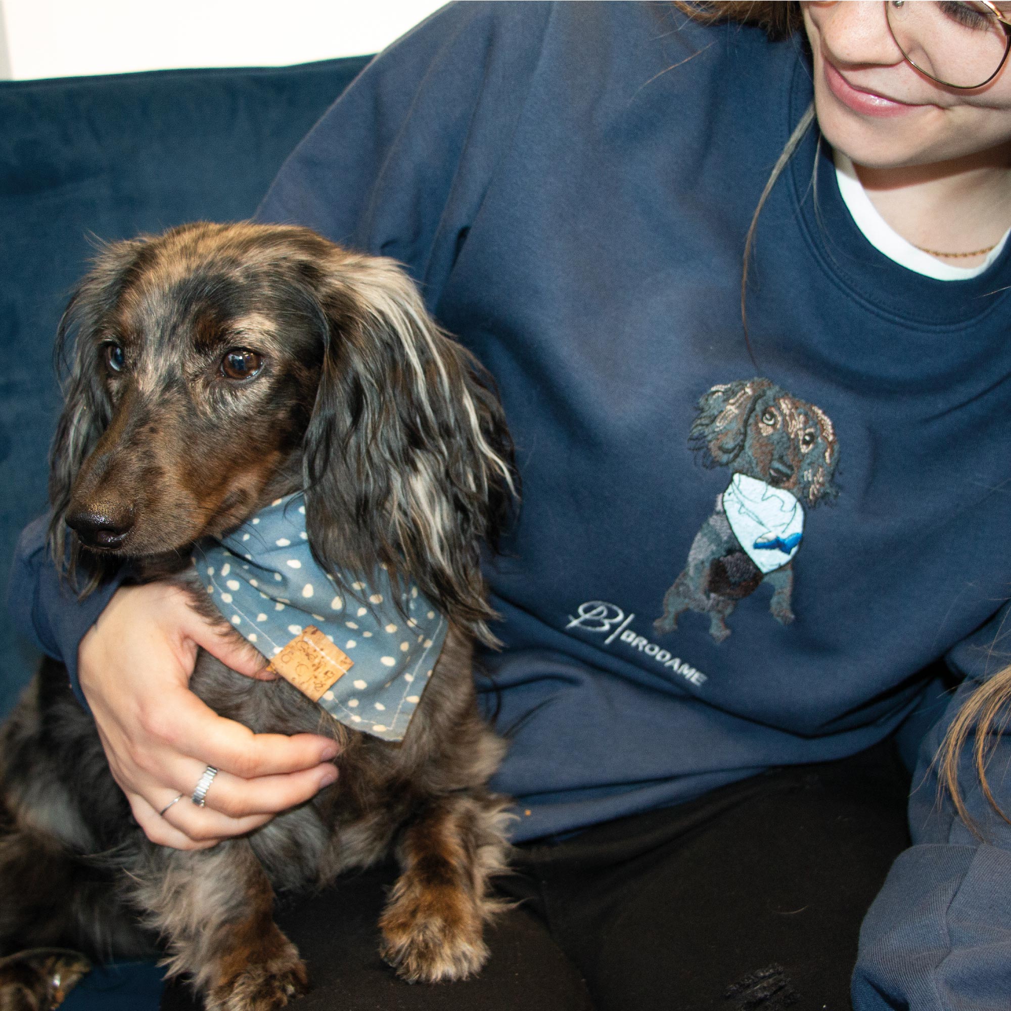 photo jeune femme avec son chien saucisse portant un coton ouaté à col rond avec une broderie réaliste de son chien