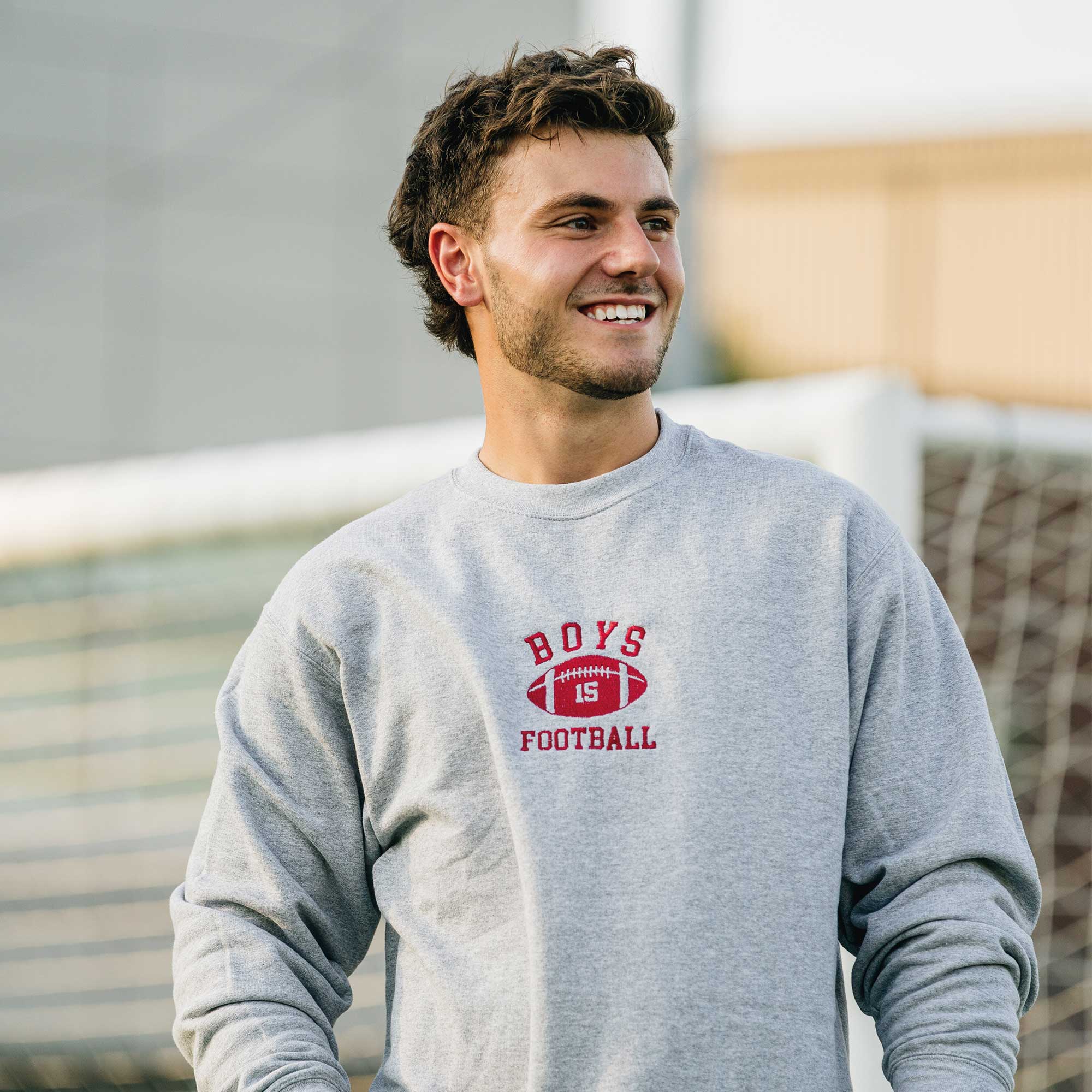 jeune homme portant un crewneck gris pâle avec une broderie boys football