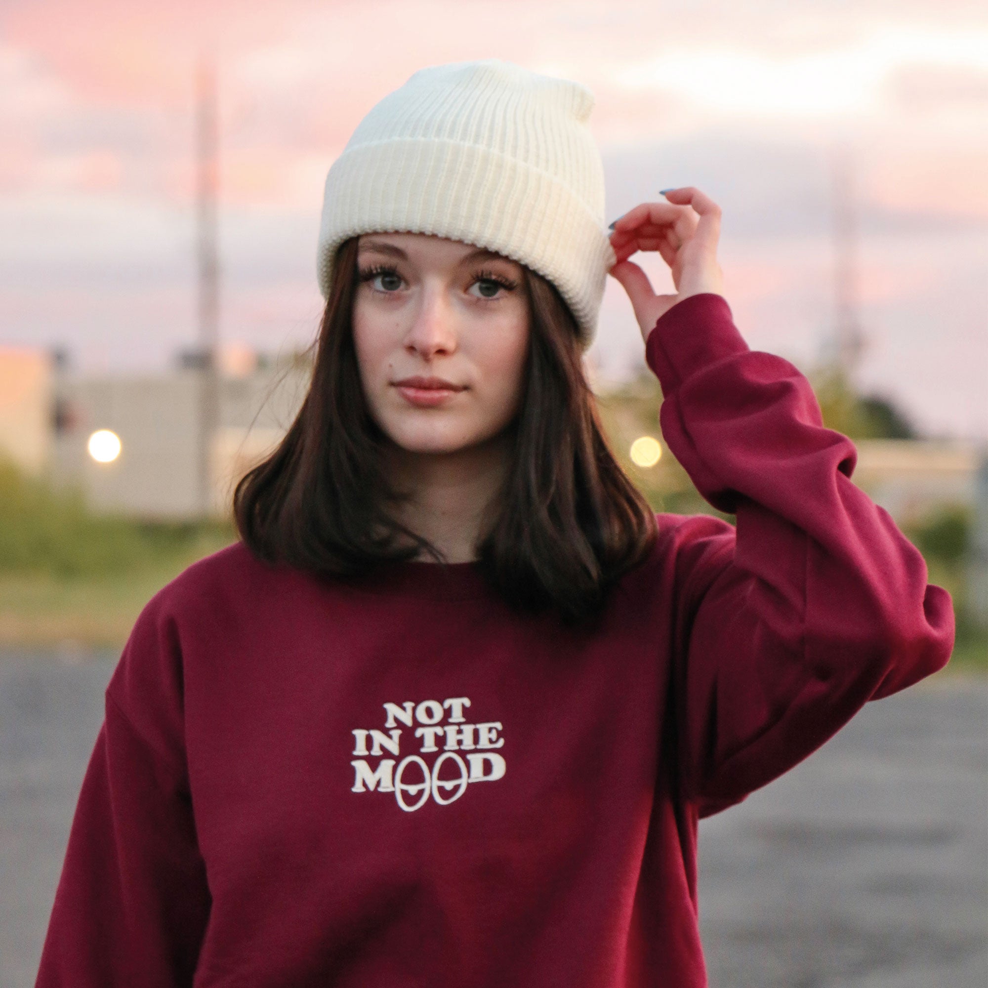 photo d'une jeune femme portant un crewneck bourgogne avec une broderie "not in the mood" et une tuque couvrant les oreilles de couleur crème, blanc cassé