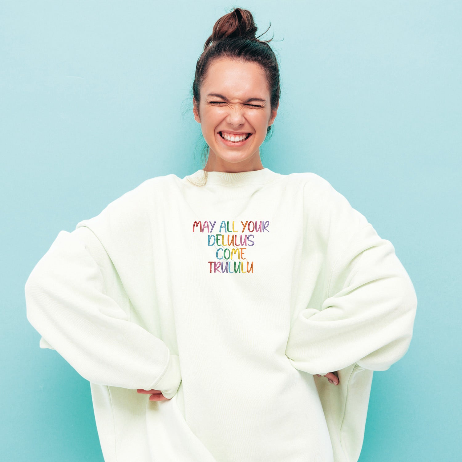 photo lifestyle d'une jeune femme aux cheveux brun portant un crewneck blanc oversized brodé "may your delulus come trululu" multicolore