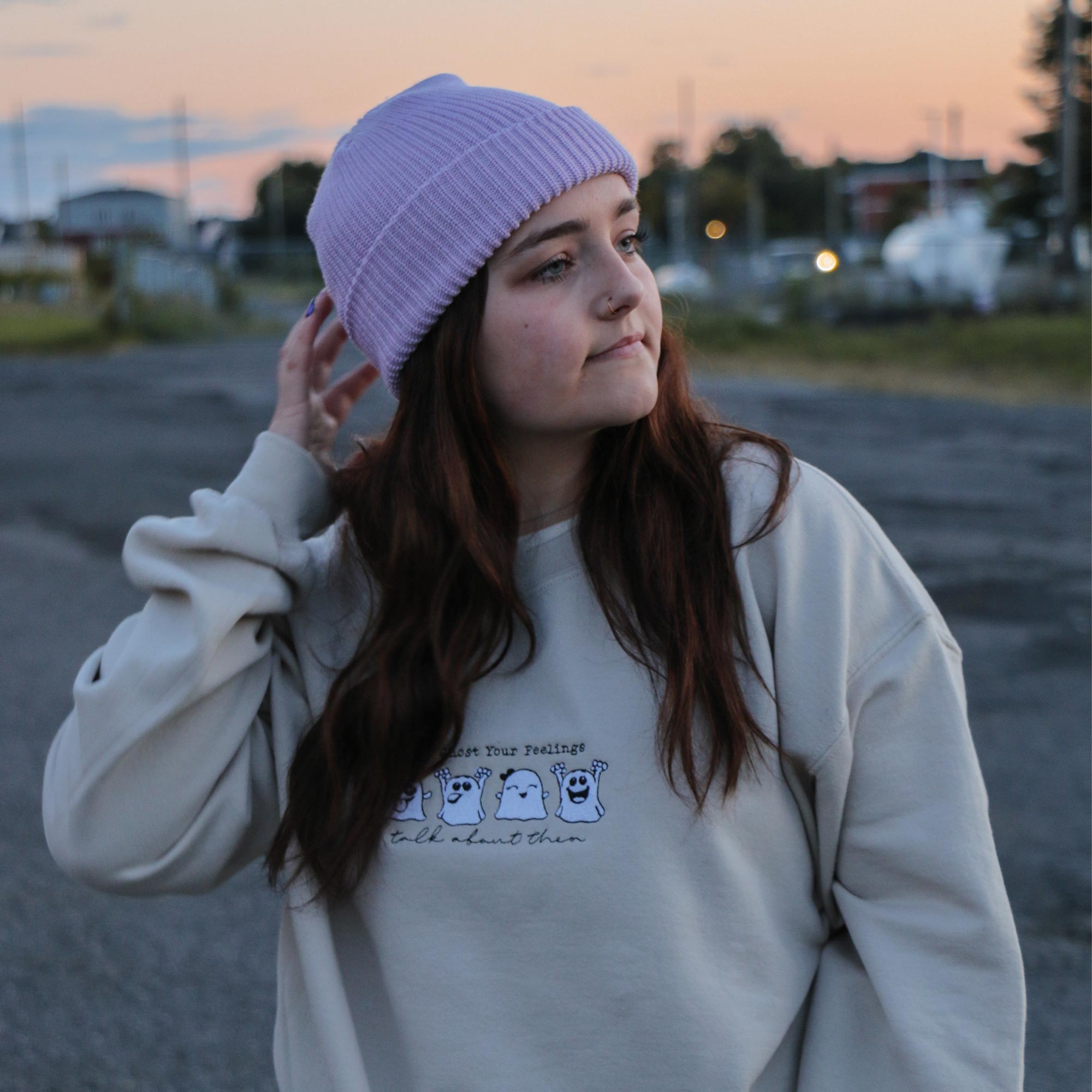 photo lifestyle d'une jeune femme au cheveux bruns portant un crewneck beige et une tuque lavande au coucher du soleil