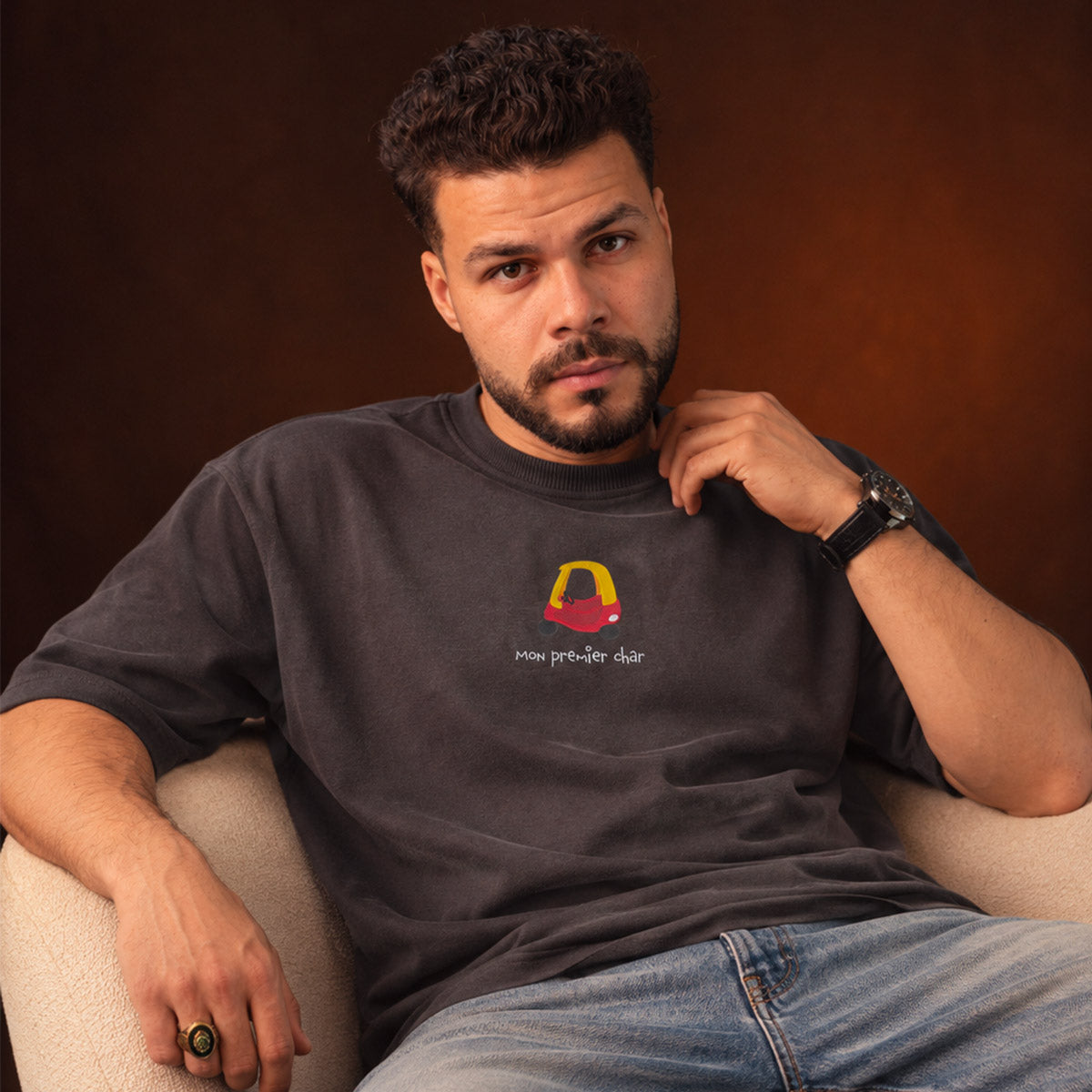 photo d'un homme aux chebeux frisés portant un t-shirt à manches courte heavyweight oversized avec une broderie de voiture en jouet pour enfant