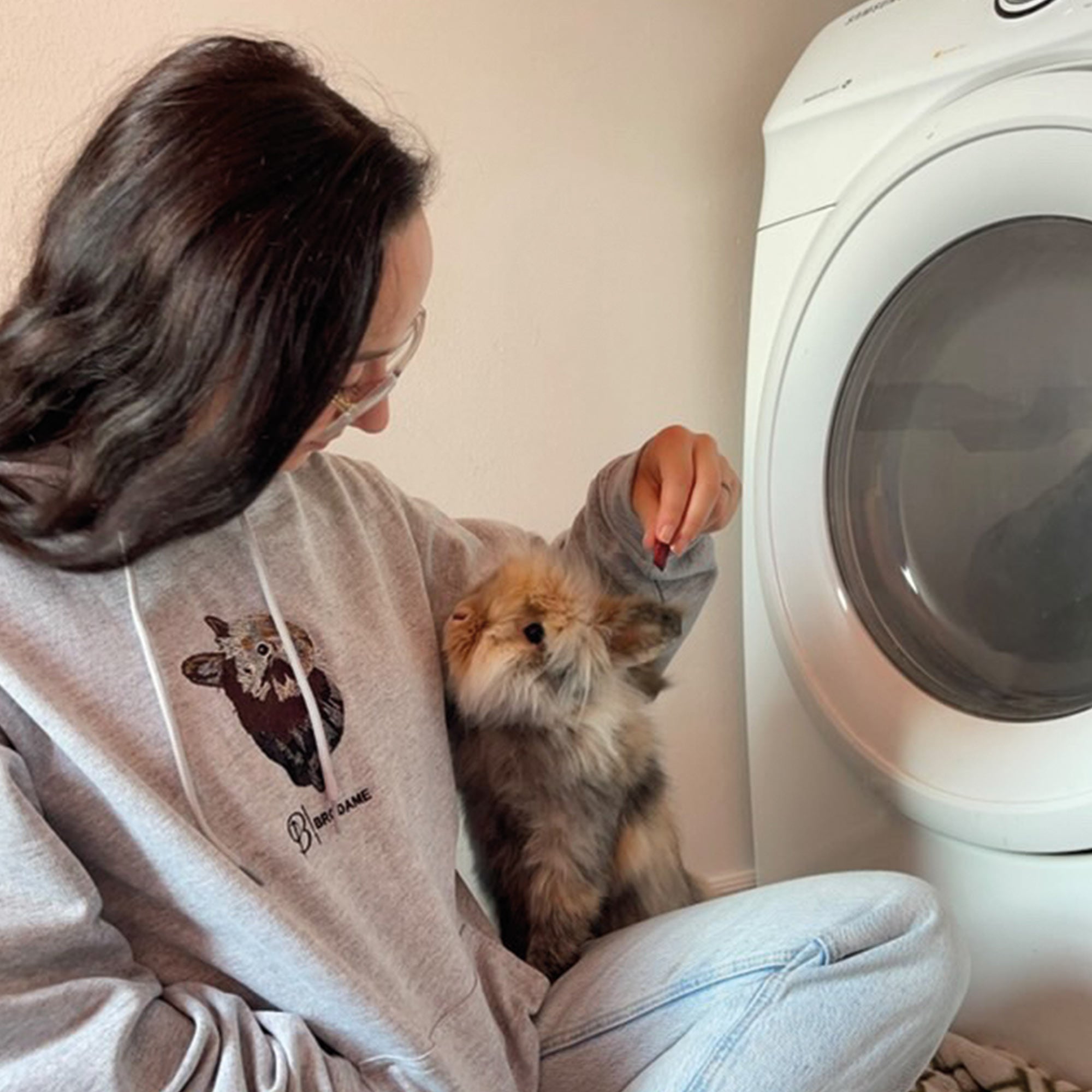 photo d'une jeune femme aux cheveux bruns portant un hoodie gris pâle avec son lapin brodé de façon réaliste avec le logo brodame en dessous.