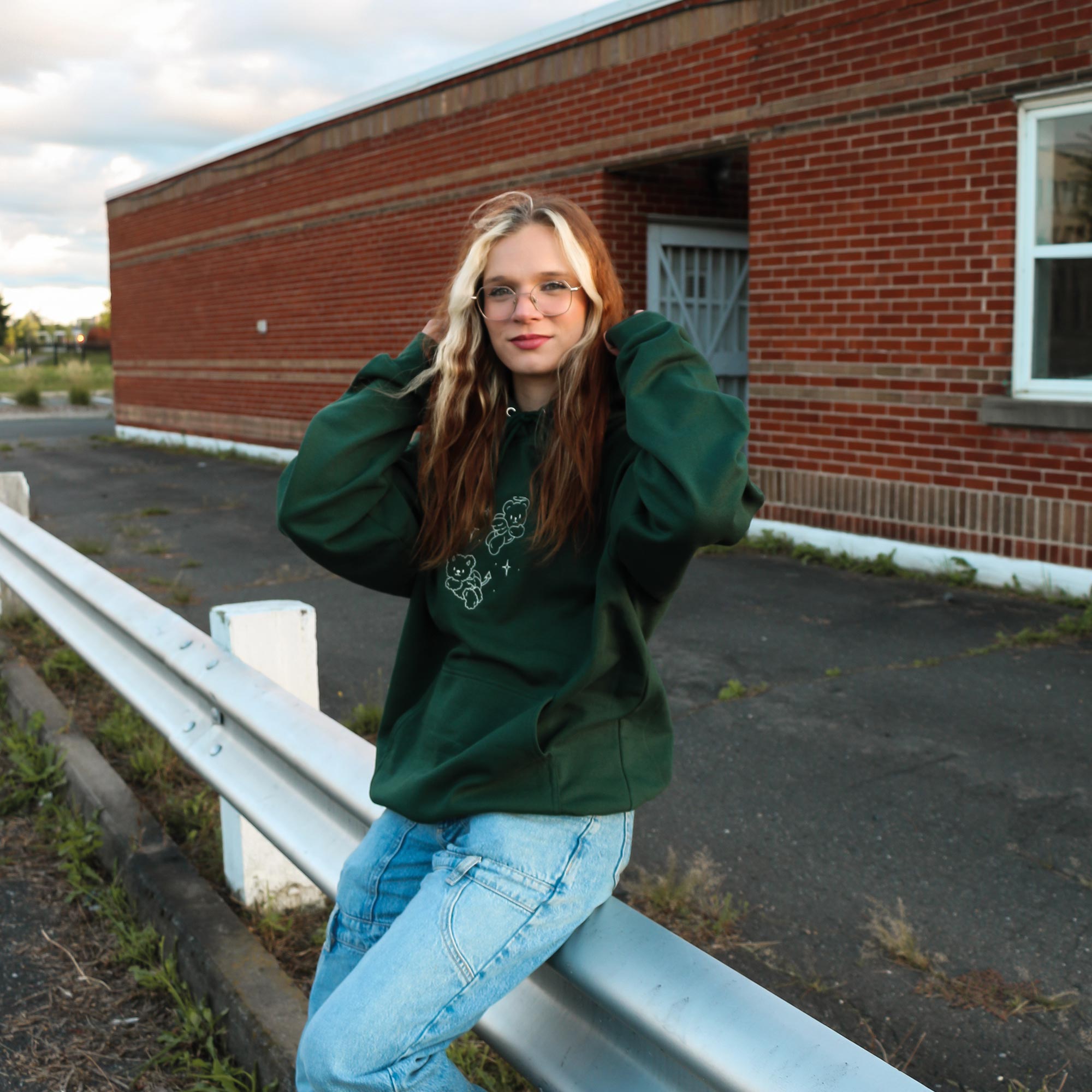 photo lifestyle d'une jeune femme portant un hoodie de couleur vert foret avec une broderie de petits oursons ange et demon en blanc crème