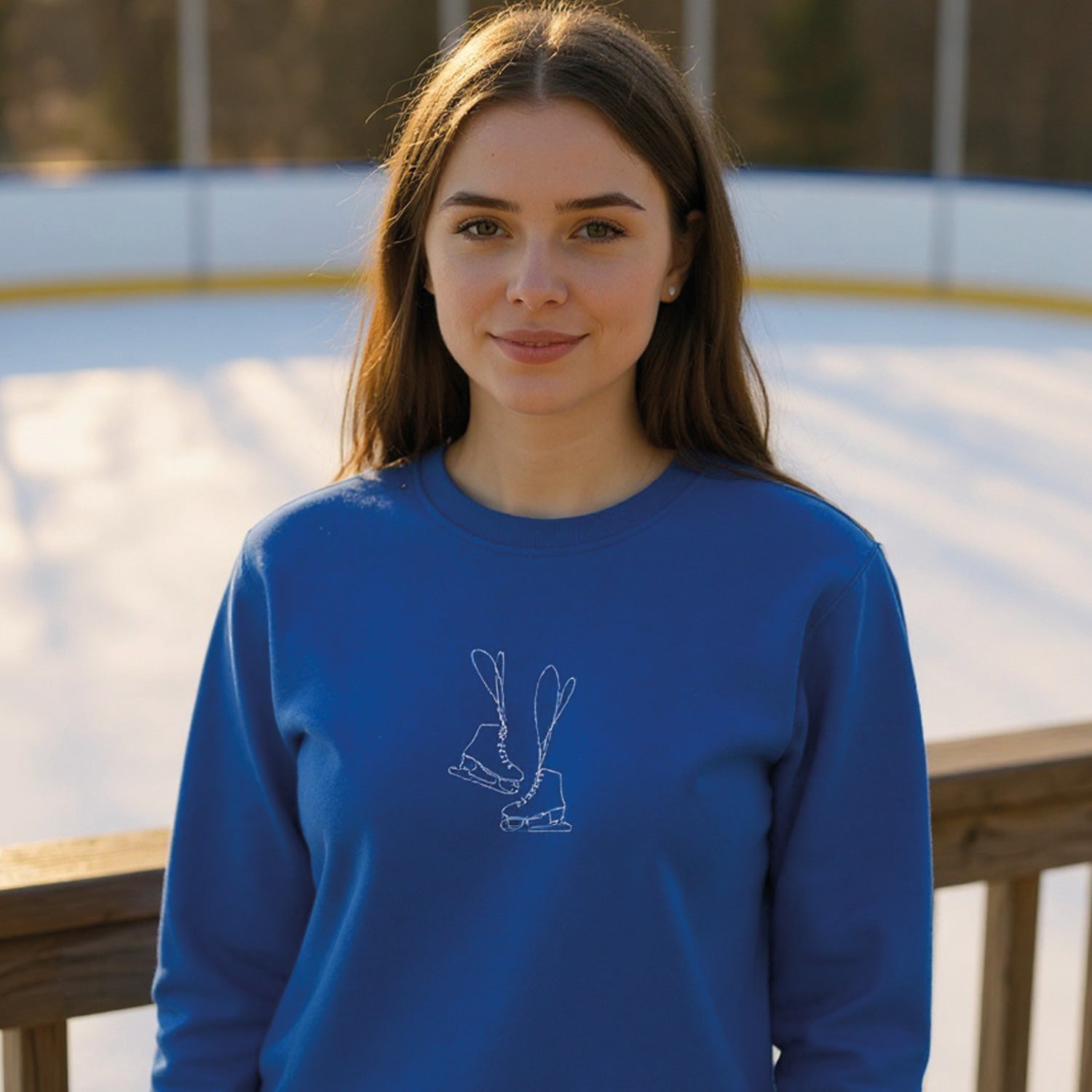 jeune femme aux cheveux bruns portant un coton ouaté à col rond bleu royal ayant une broderie minimaliste de patins de femmes en blanc