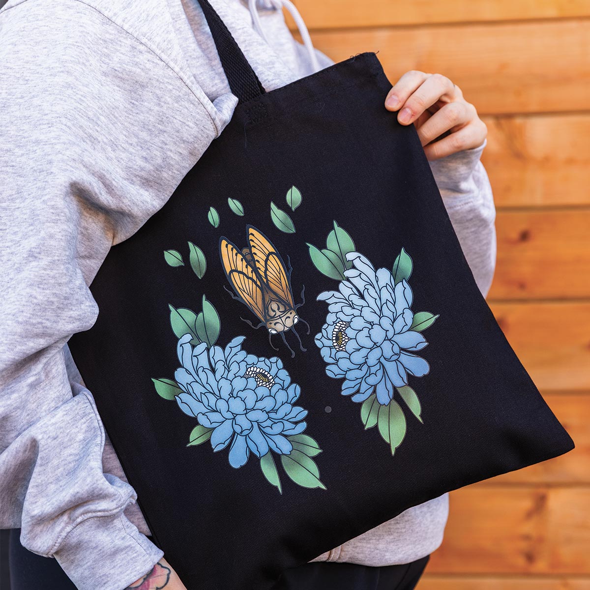 photo plan rapproché d'un sac fourre-tout noir ayant une impression de fleurs bleue et d'un insecte tenu par une jeune femme