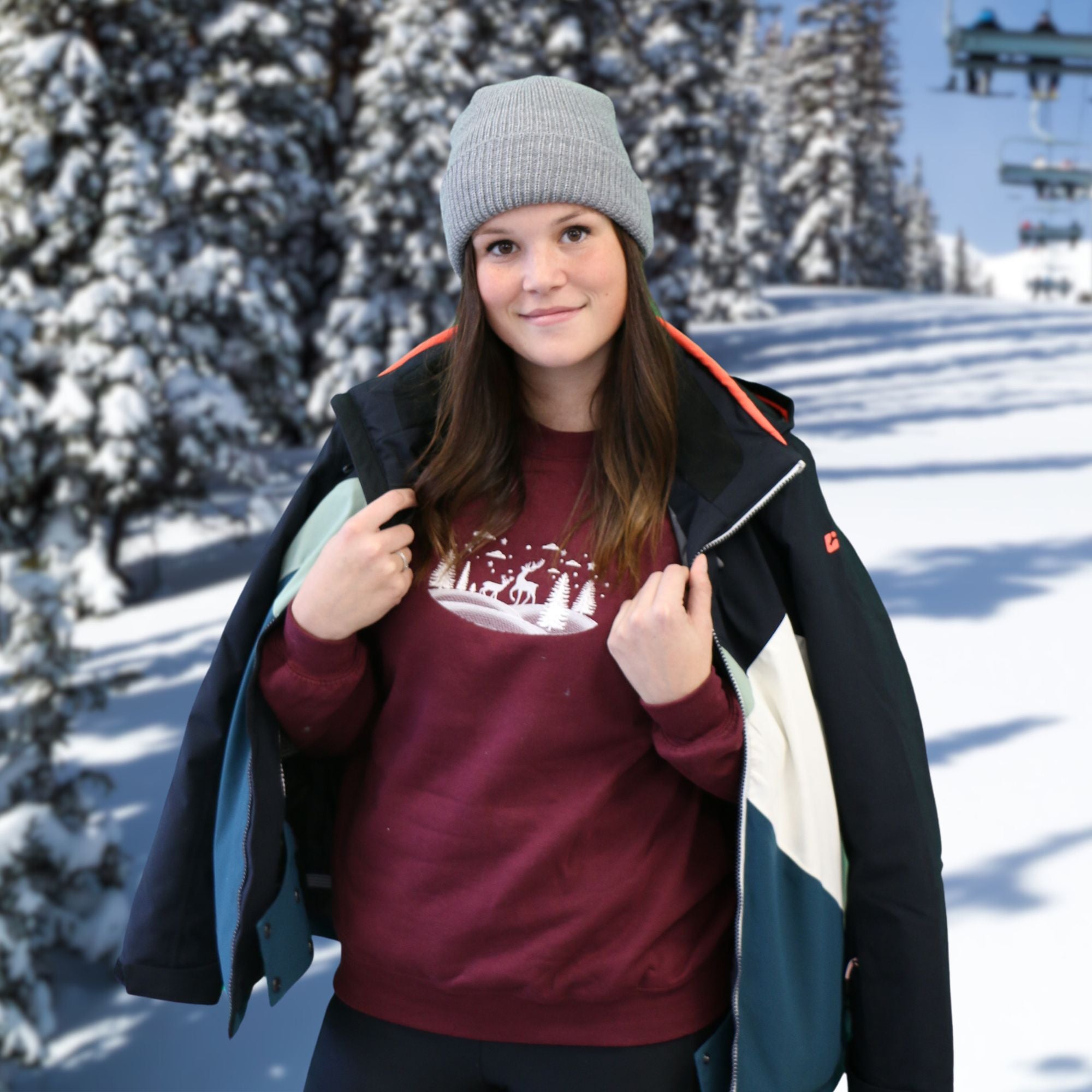 photo d'une jeune femmeportant un crewneck bourgogne avec une broderie blanche de paysage d'hiver dehors avec de la neige