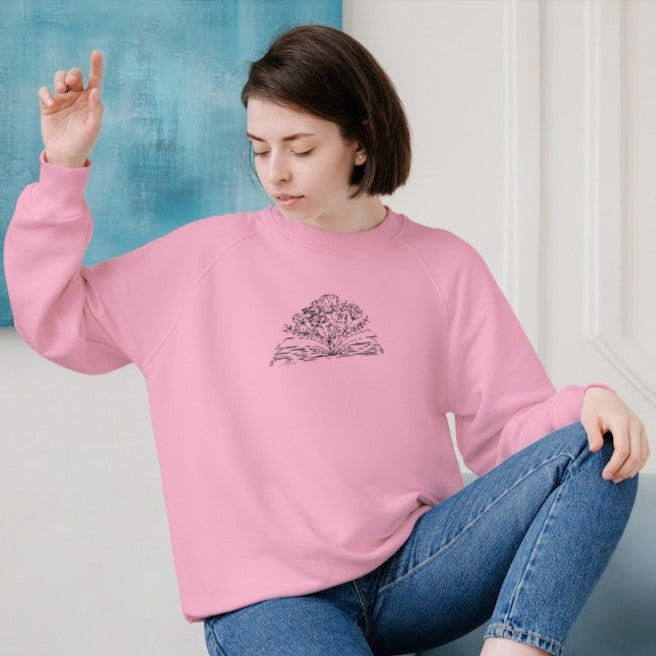 crewneck rose pâle brodé avec un livre et des fleurs minimalistes