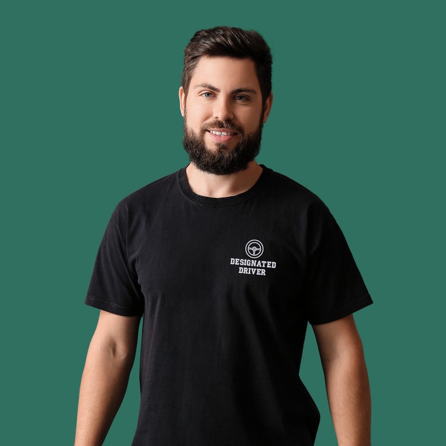 jeune homme blanc avec une barbe brune portant un t-shirt noir avec une broderie "designated driver" au coeur, en blanc