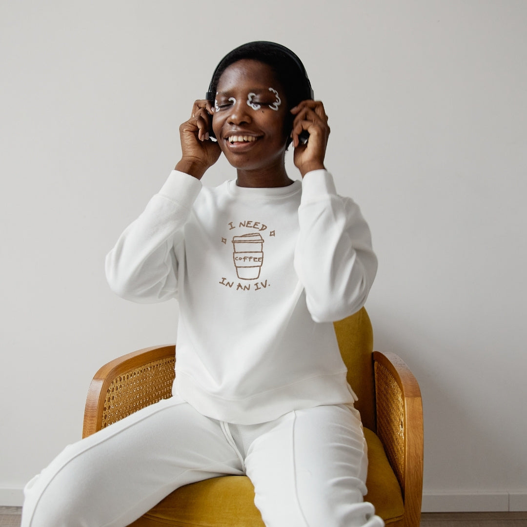 photo d'une femme noire écoutant de la musique en portant un crewneck blanc avec une broderie de café brune centrée sur le chandail