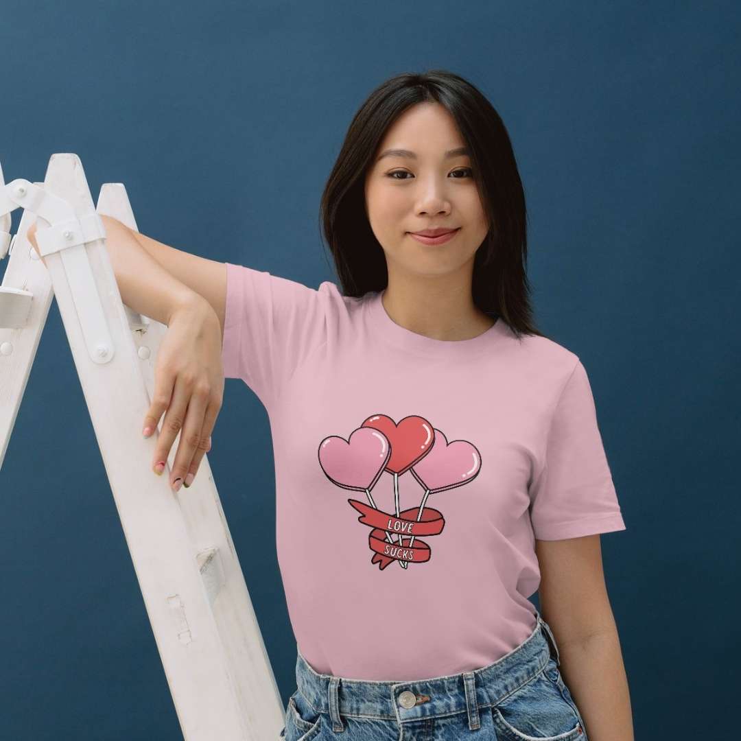 photo lifestyle d'une jeune femme asiatique portant un t-shirt rose pâle imprimé avec des sucettes en forme de coeur et l'inscription "love sucks"